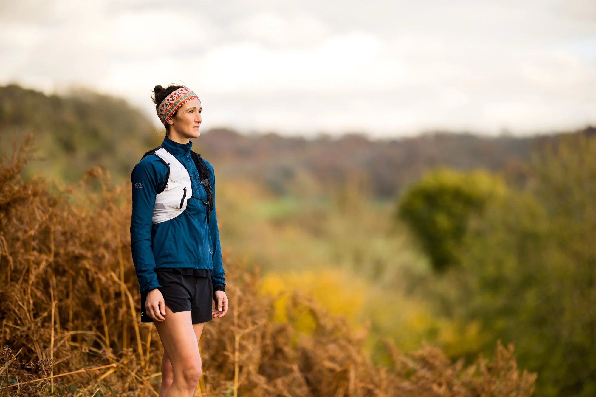 Person in outdoor gear standing on a trail with autumn foliage.