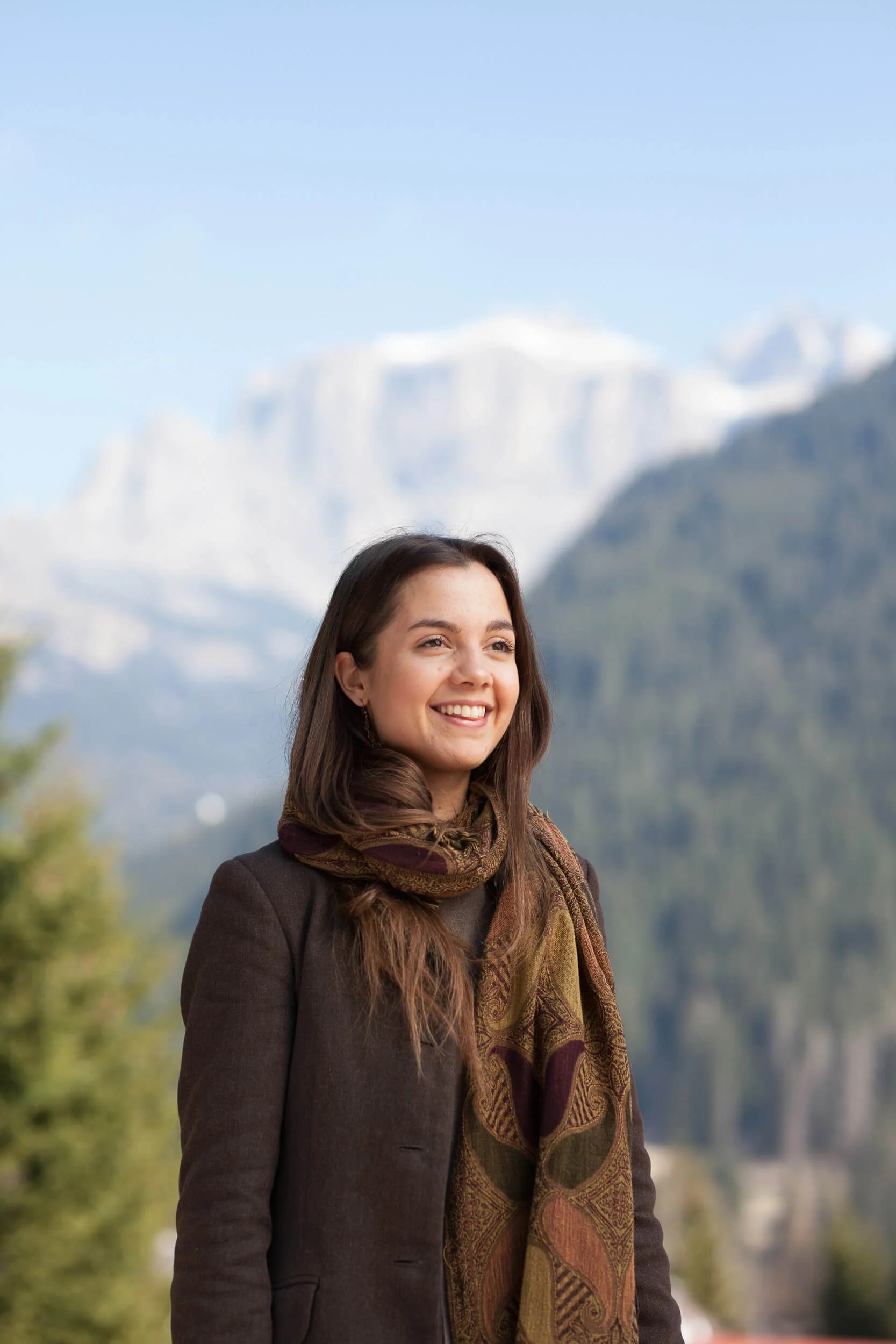 A woman smiling in front of a mountainous landscape.