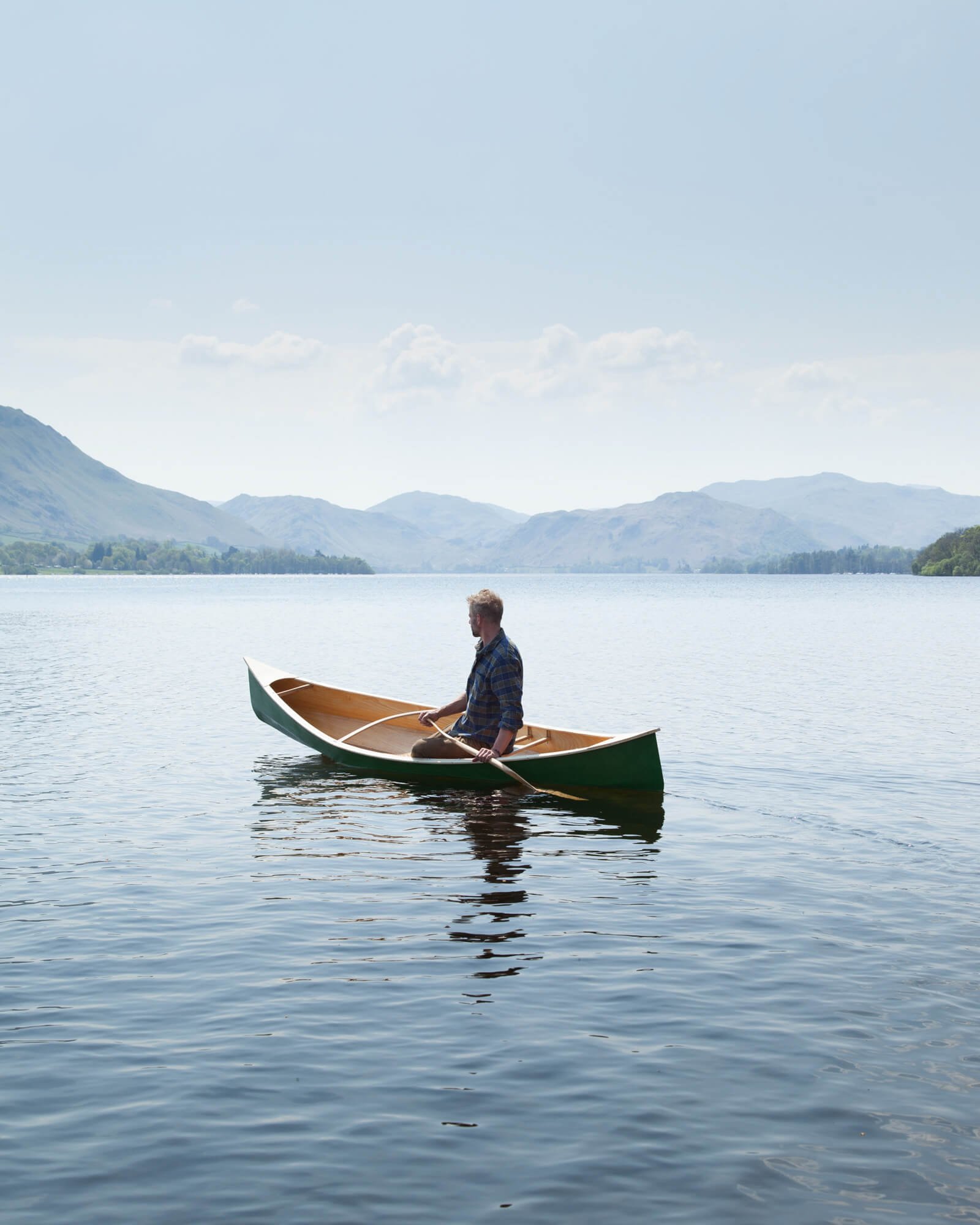 Person canoeing on a calm lake with mountains in the background under a clear sky.
