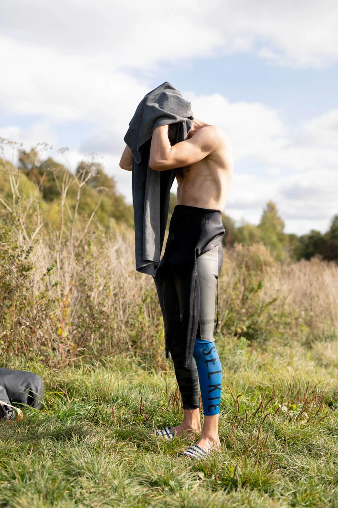Person changing outdoors, wearing Selkie branded leggings, holding a shirt.