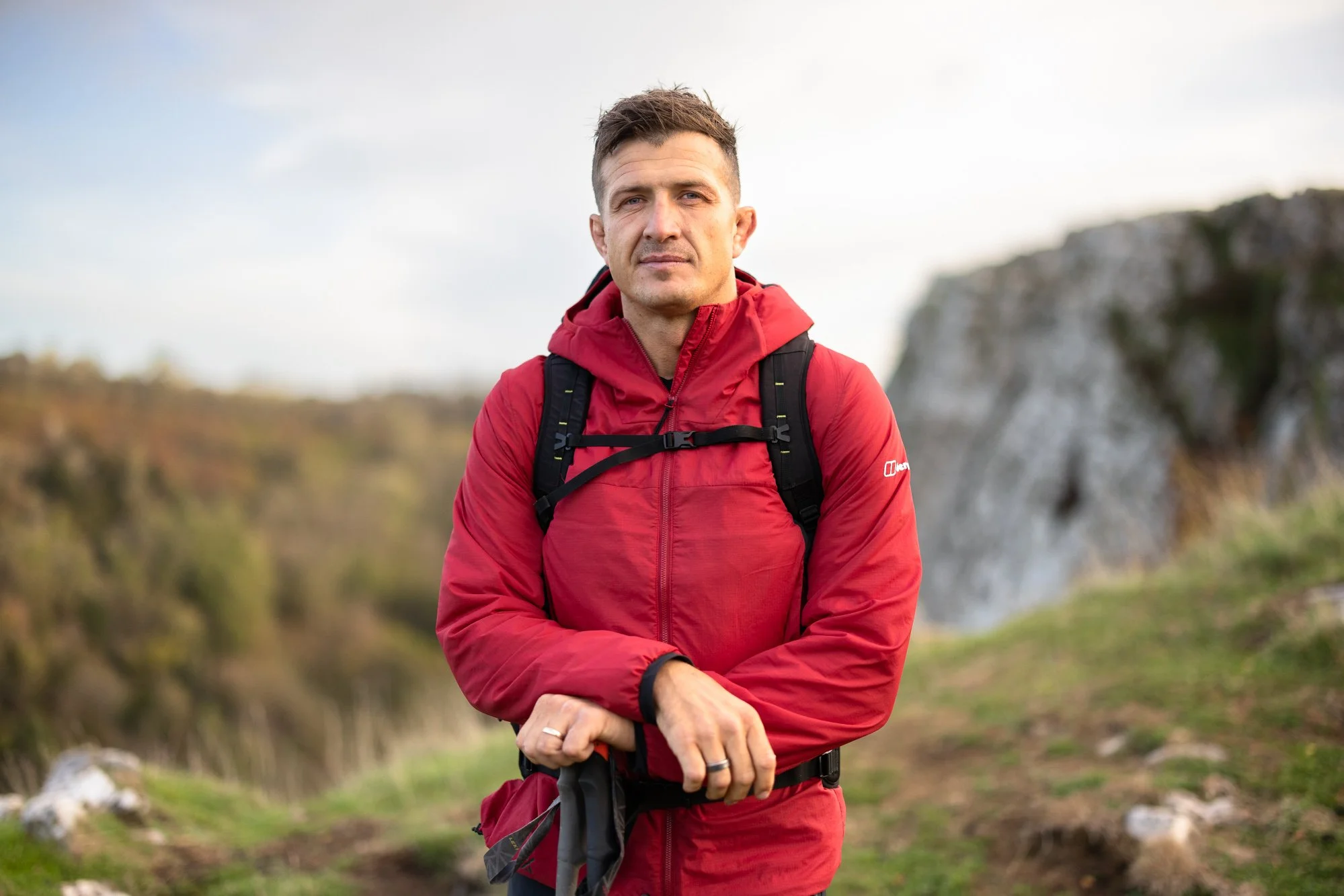 Ed Jackson in red jacket standing outdoors on a hiking trail with a backpack.