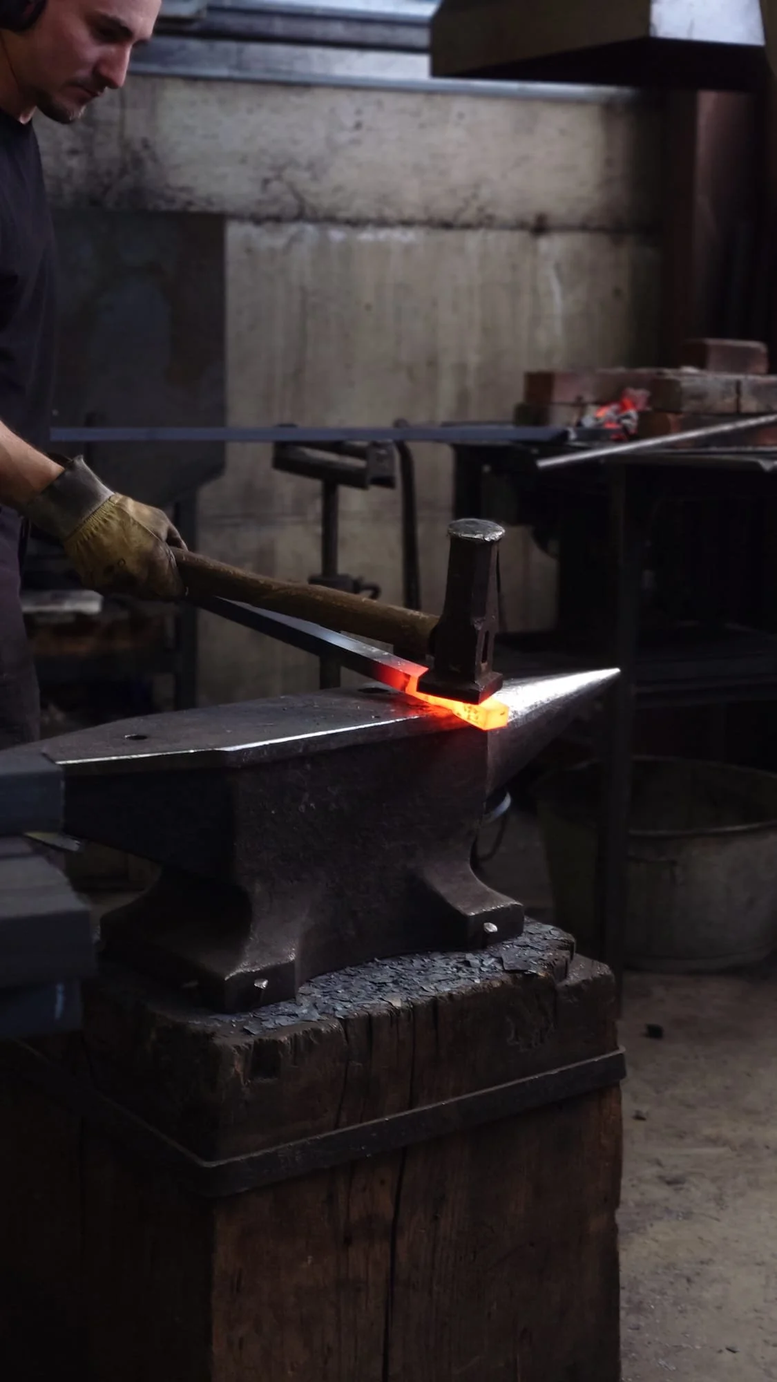 Un forgeron frappe un fer chaud sur une enclume dans un atelier de forge.