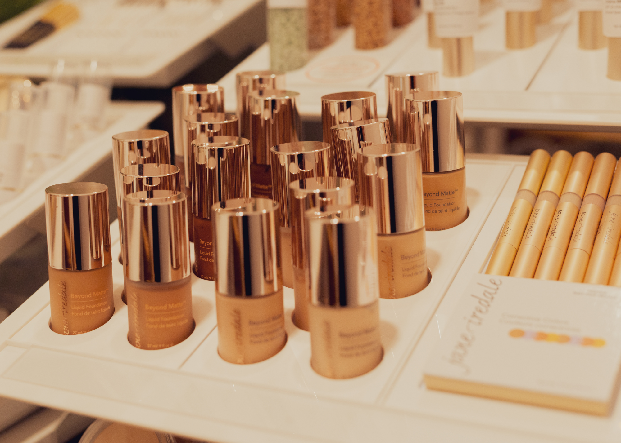 Display of liquid foundation bottles with rose gold caps on a store shelf.