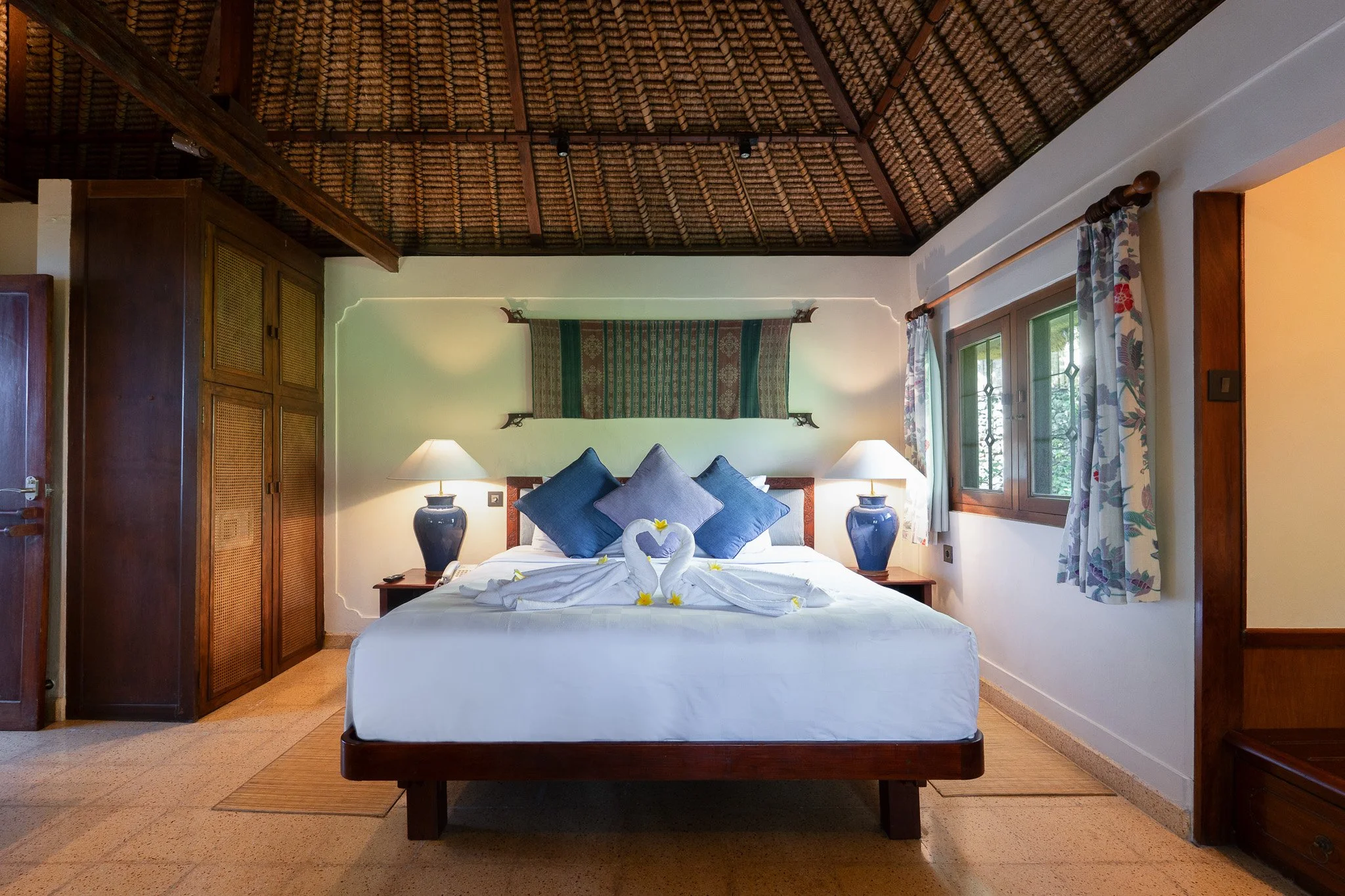 Two swans made from towels sit on a comfortable teak wood bed in a thatched cottage in a balinese designed bedroom