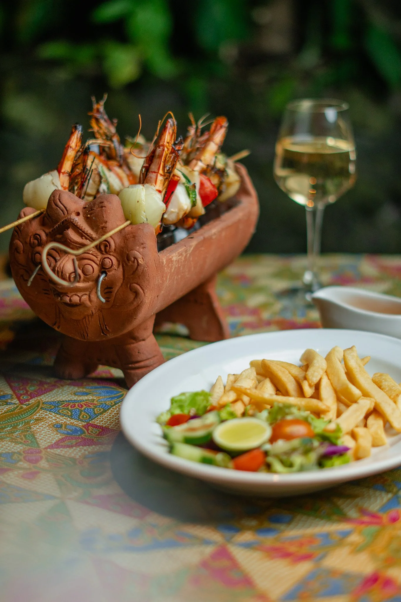 Large prawns sit in a terracotta boat next to a plate of chips with salad
