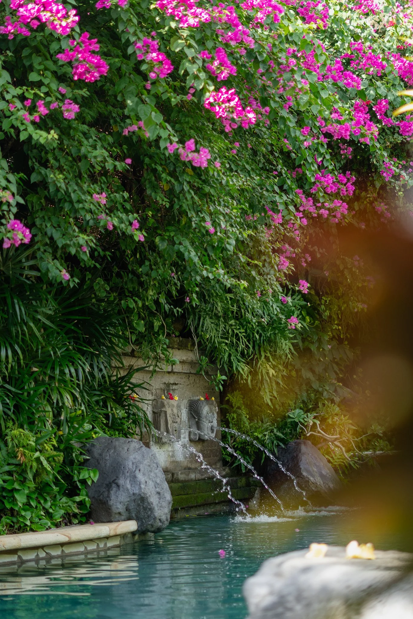 A fountain made of three stone carved heads flow water into the pool.