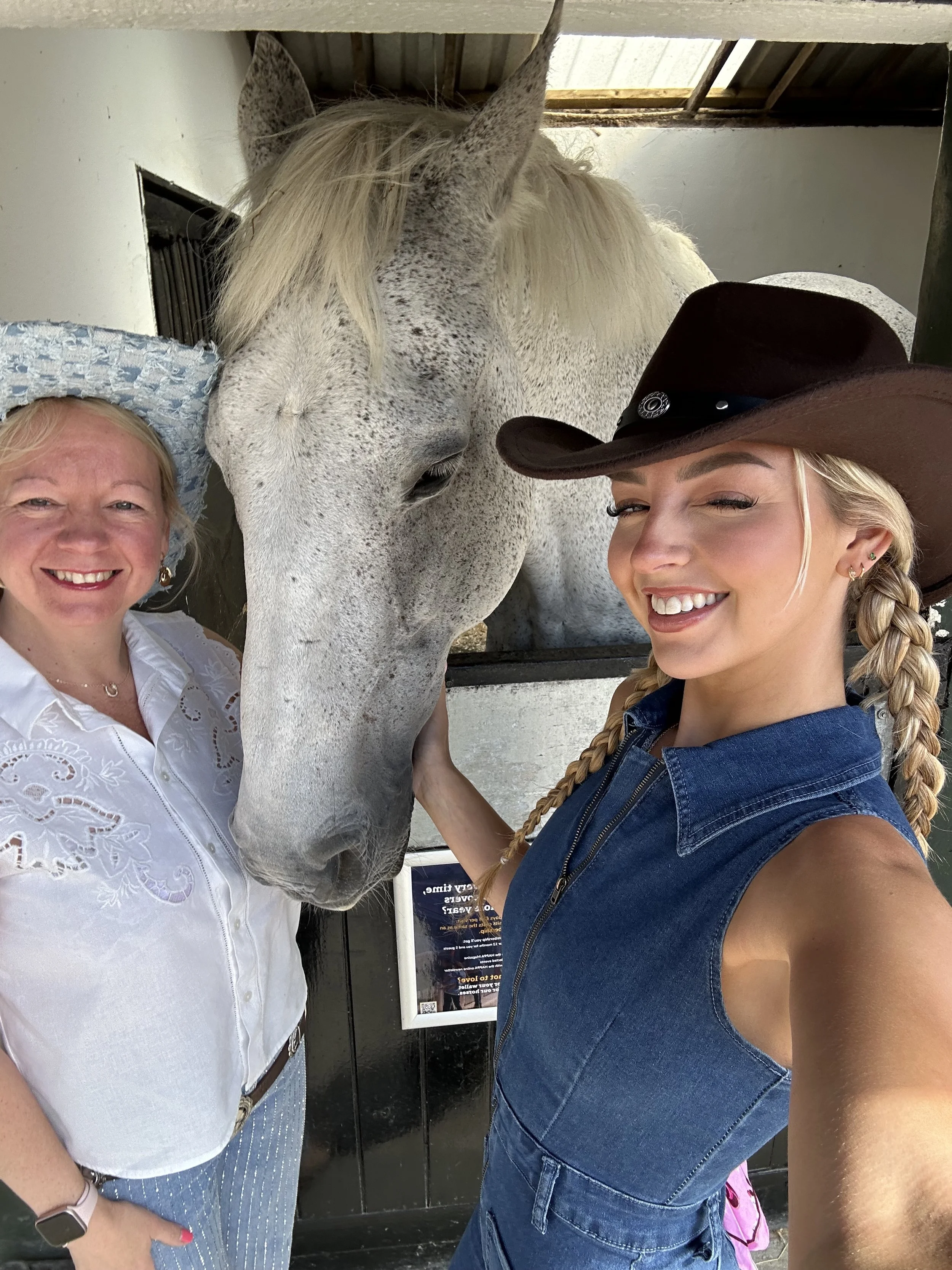 Two women and a gray horse with white mane and speckled coat smiling for a selfie.