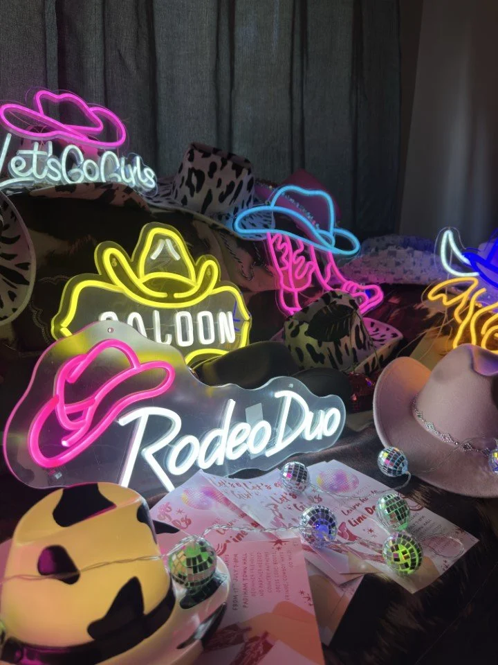 Neon signs with cowboy hat and hat with cow print patterns, along with small disco balls on a table.