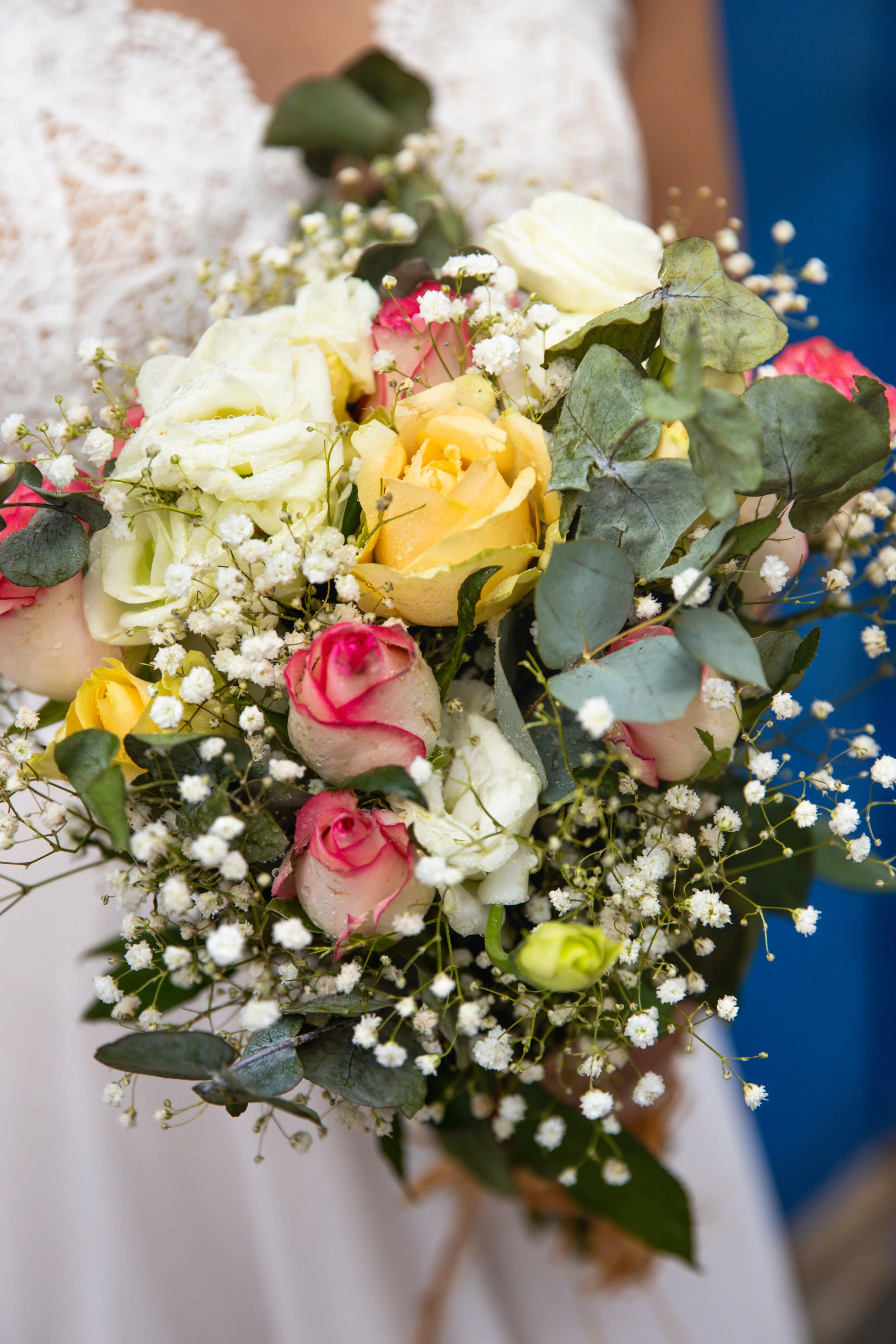 A bridal bouquet with white, yellow, and pink roses, accented with baby's breath and eucalyptus leaves.