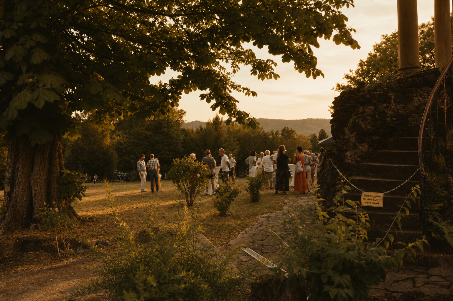 Gruppe von Menschen im Freien bei Sonnenuntergang, auf einer Wiese mit Bäumen, versammeln sich möglicherweise bei einer Veranstaltung, neben einer Steintreppe mit einem Schild, das Zutritt für Unbefugte verbietet.
