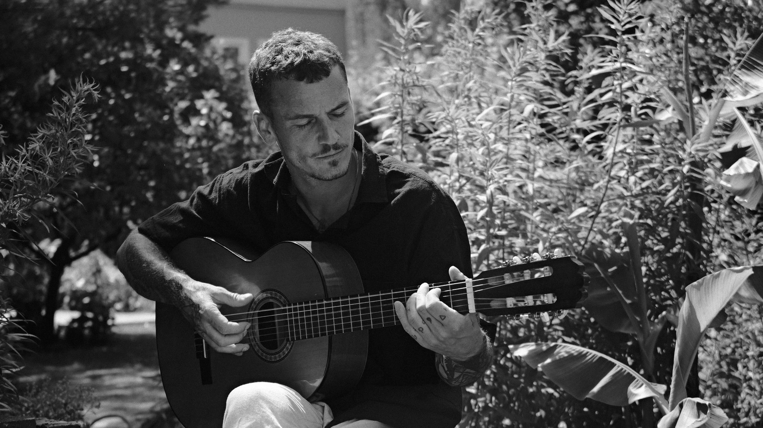 Ein Mann spielt Gitarre im Freien unter Bäumen, schwarz-weiß