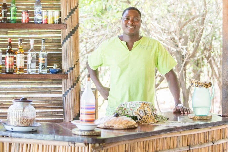 A smiling Malawian bartender serving guests at Mumbo Island on Lake Malawi.
