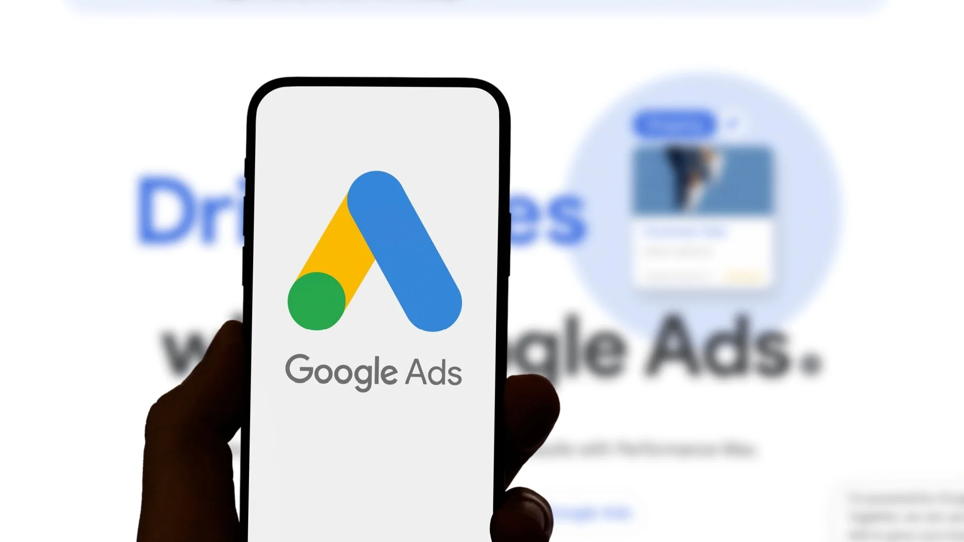 Une personne tient un téléphone affichant le logo de Google Ads, avec un fond montrant une publicité et le logo de Google Ads flous.