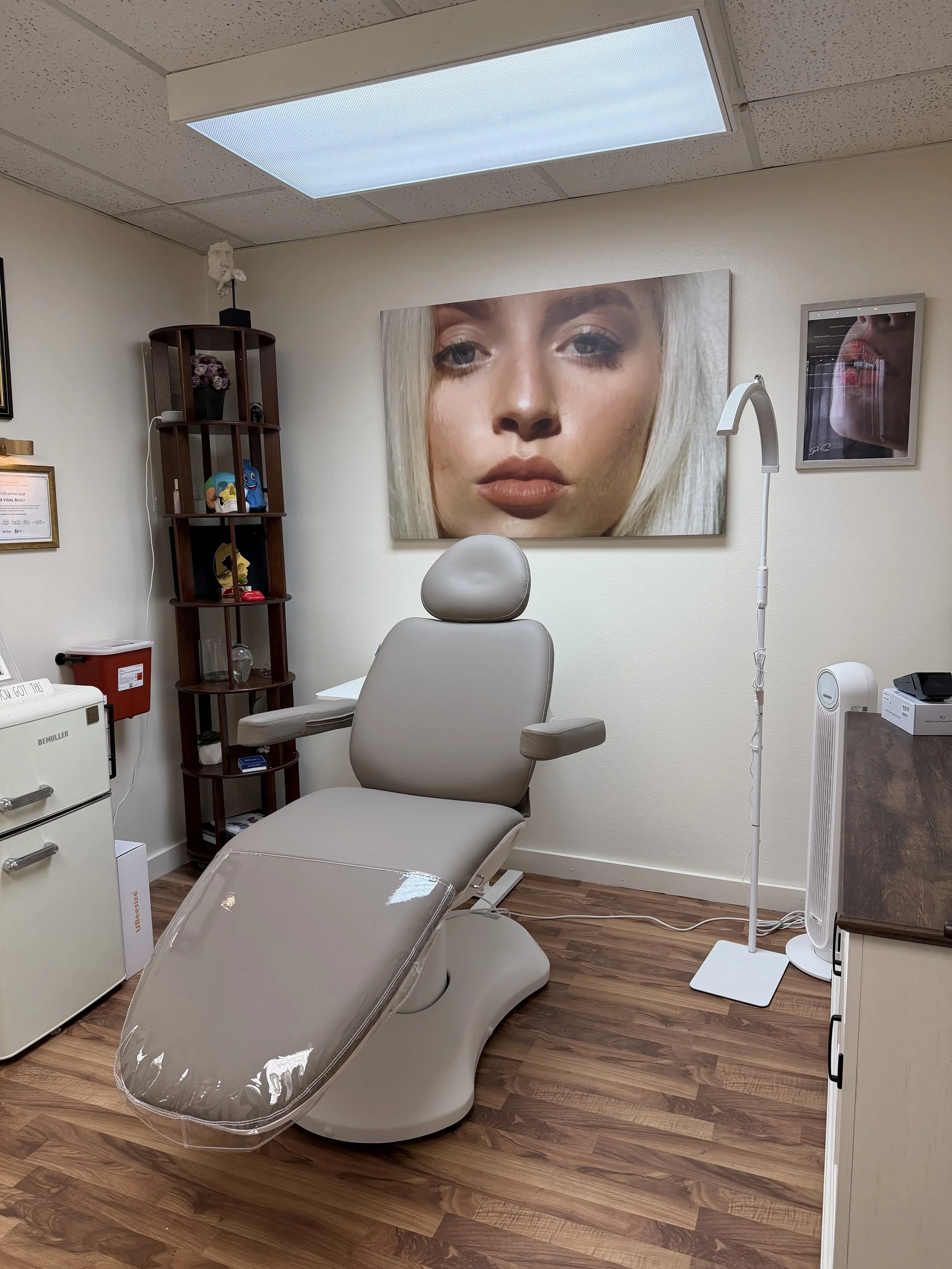 Medical examination room with dental chair, artwork of a woman's face on the wall, and medical equipment around.