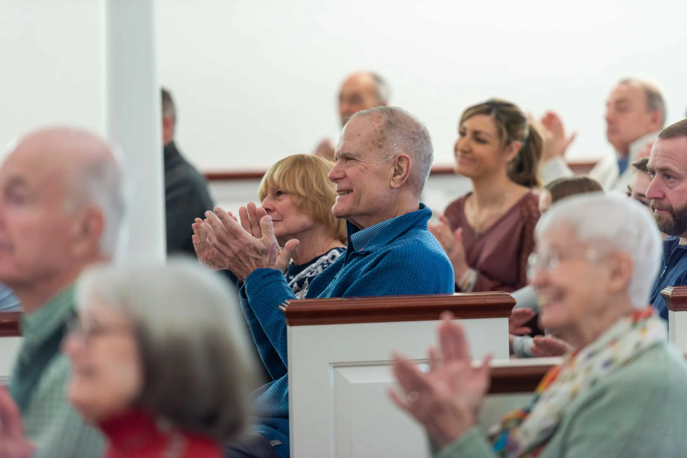 A group of people seated in a church or auditorium, clapping and smiling during a service or event.