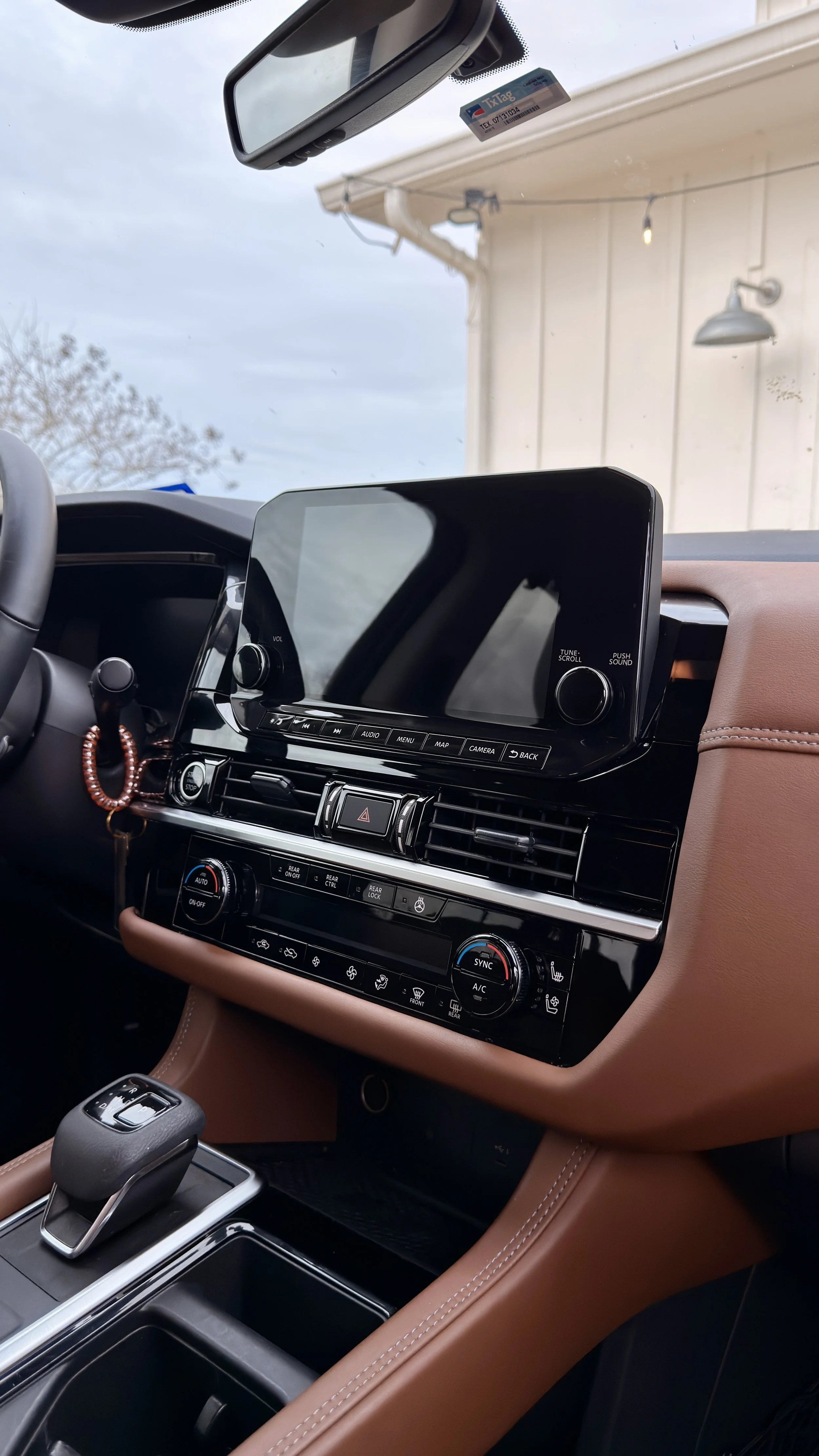 Interior of a modern vehicle showing the dashboard, center console, and steering wheel. The dashboard features a large touchscreen display, climate controls, and various buttons, with a gear shift and storage compartment in the foreground.