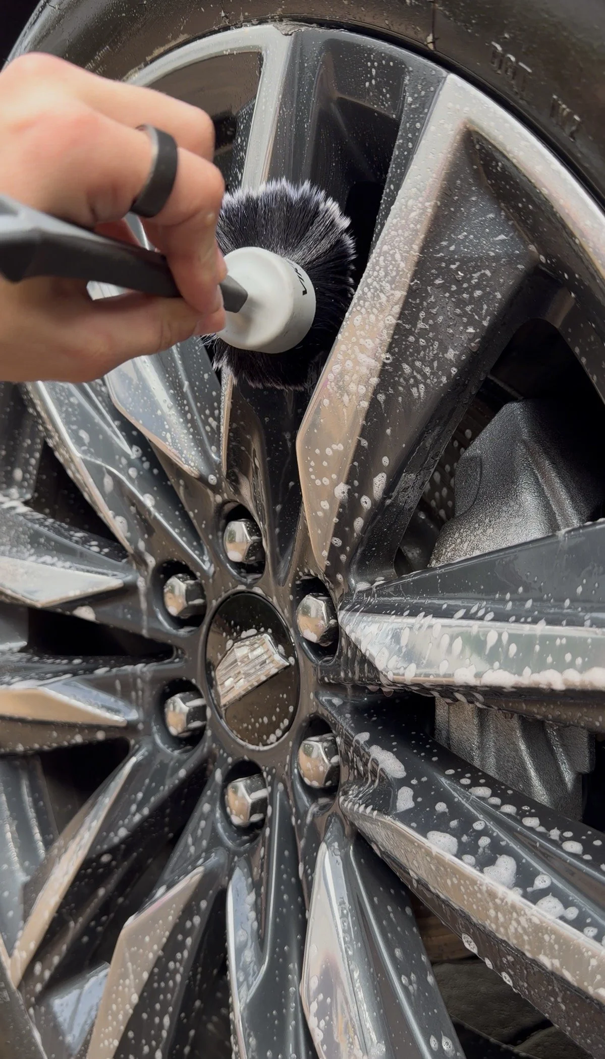 Person washing a black and silver car wheel with soap and a brush
