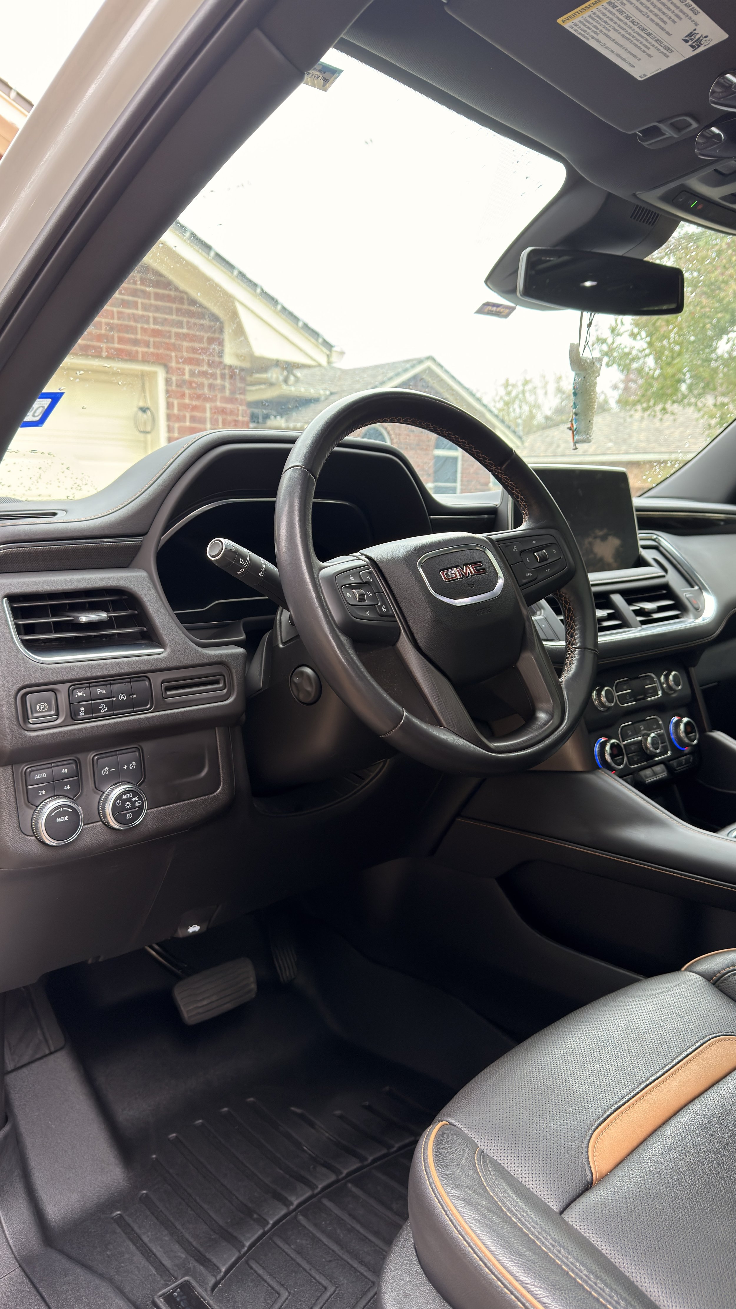 Interior of a GMC vehicle showing the steering wheel, dashboard, control buttons, climate controls, and part of the front passenger seat.