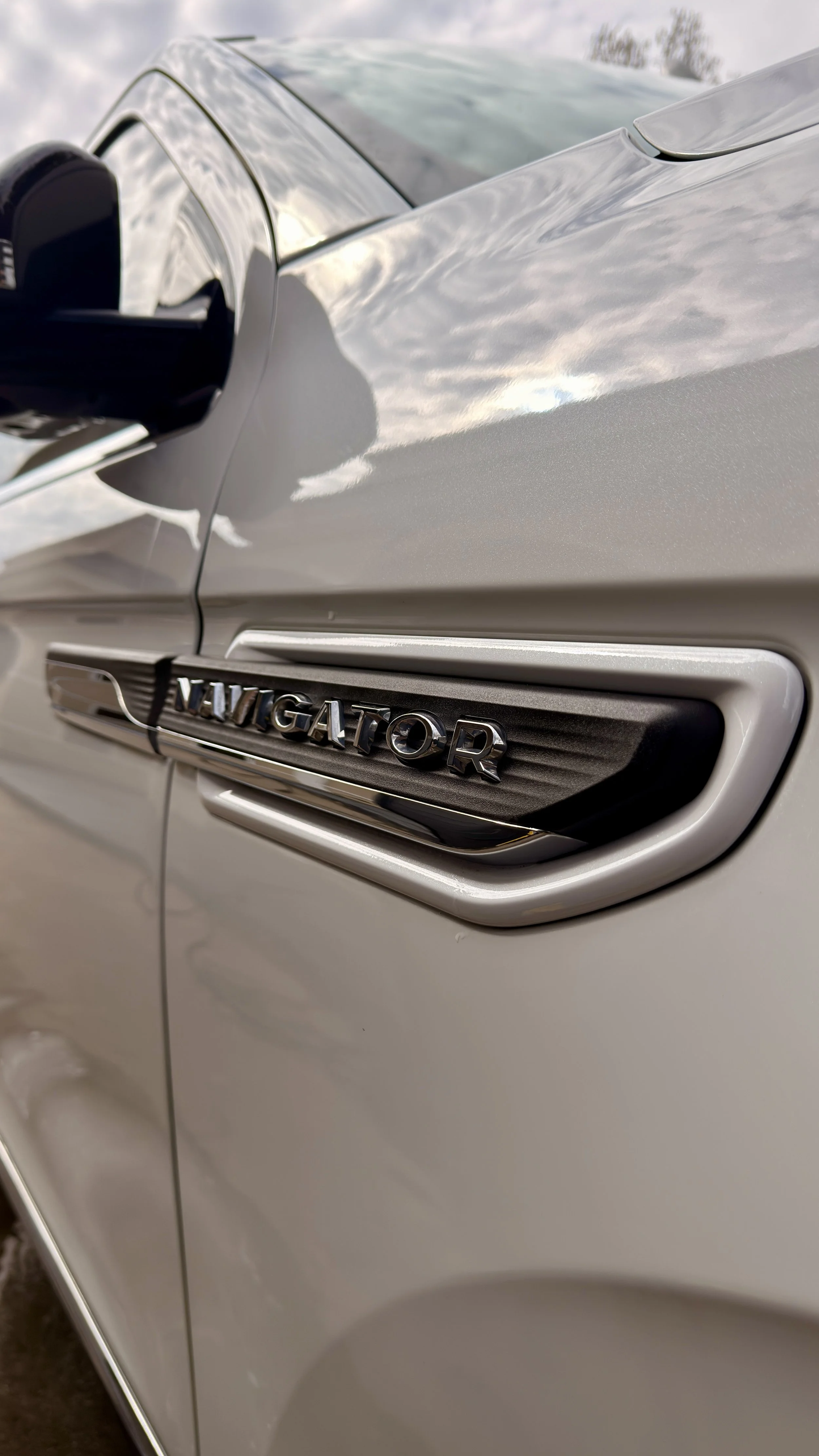 Close-up of a white vehicle with a chrome 'Navigator' badge on the side.