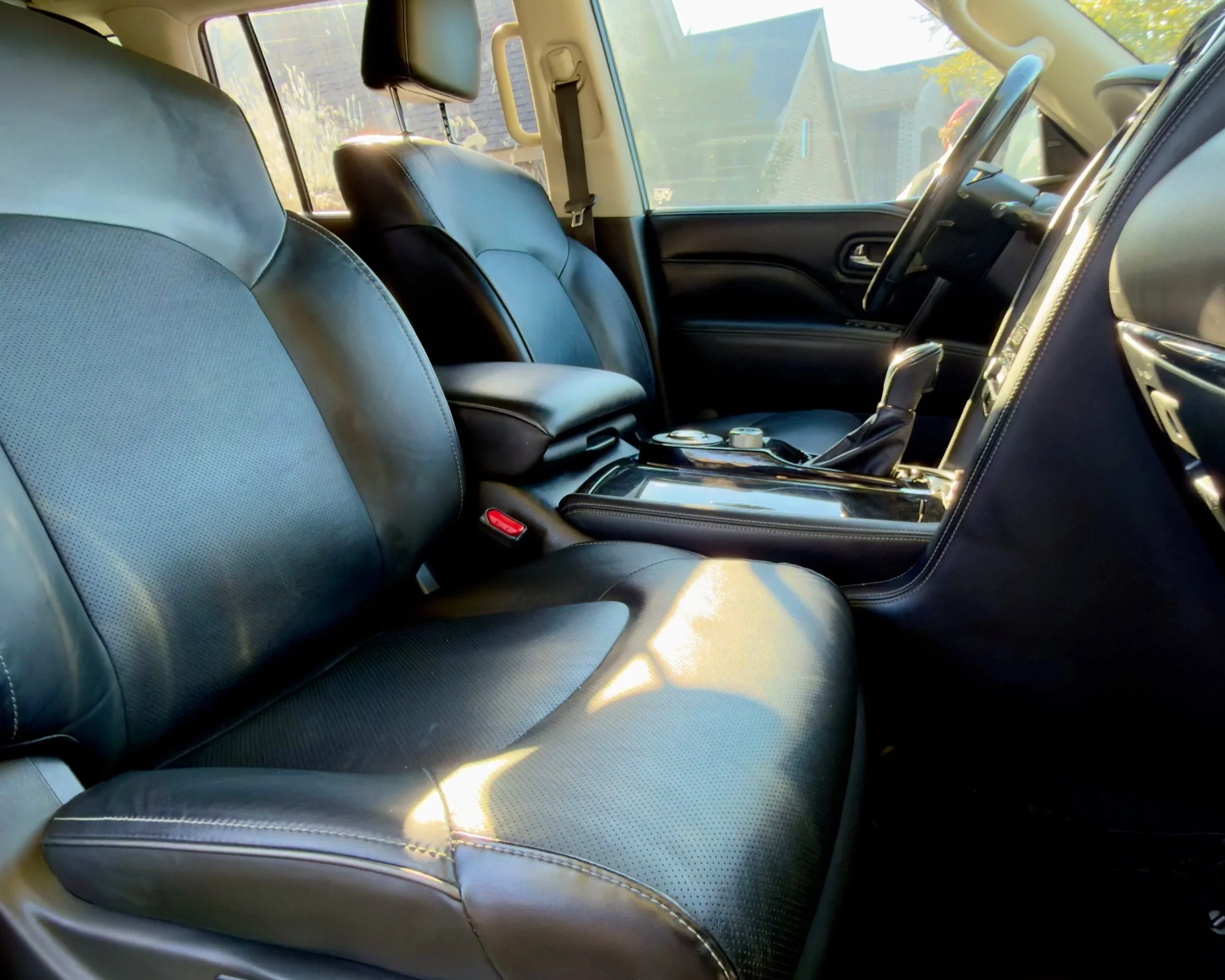 The interior of a car showing black leather seats, a dashboard, console, and steering wheel, with sunlight coming through the windows.