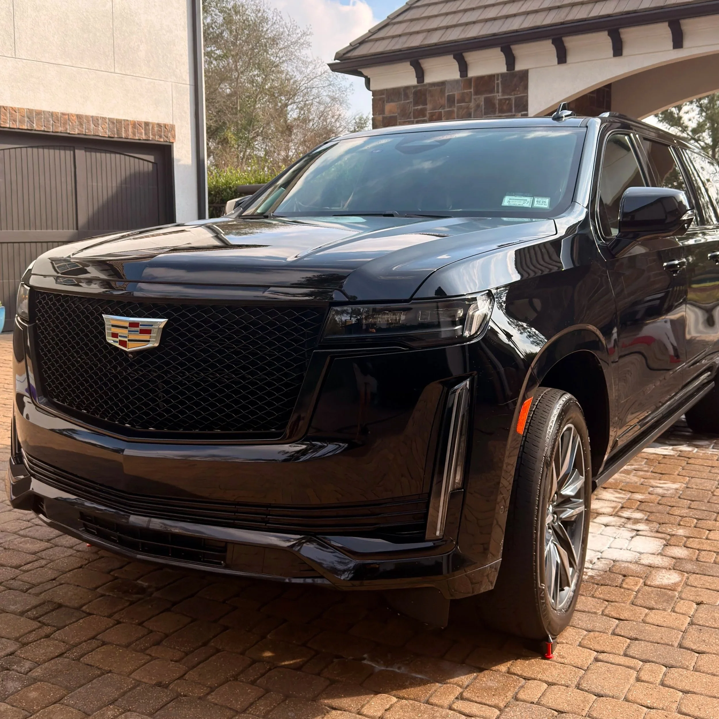 A black Cadillac SUV parked on a brick driveway in front of a house with a garage.