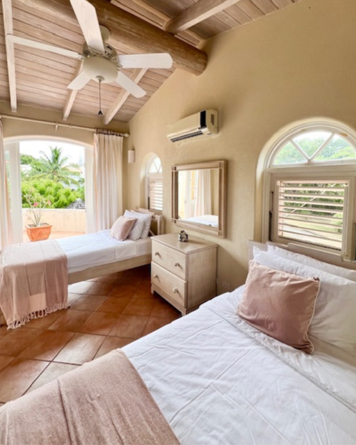 Bedroom with two twin beds, beige walls, wooden ceiling, ceiling fan, air conditioner, mirror, dresser, and window with shutters
