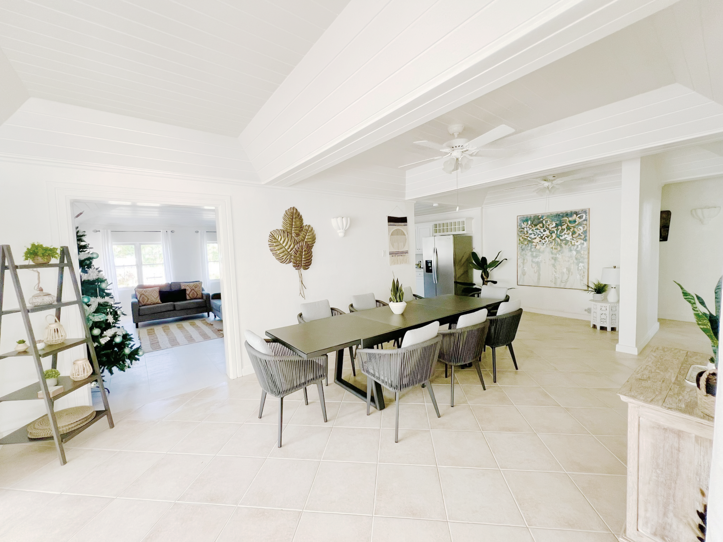 Interior of a bright, modern dining room and living space with white walls and ceiling, a black dining table with six chairs, plants, and wall decorations.