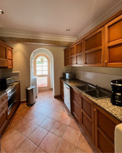 Kitchen with wooden cabinets, granite countertops, a double sink, stove, microwave, coffee maker, and tile floor, small window with decorative arch and blinds.