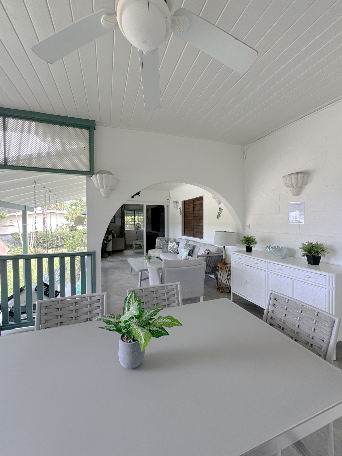 Indoor patio with white ceiling fan, white furniture, potted plants, and decorative shells on the wall.