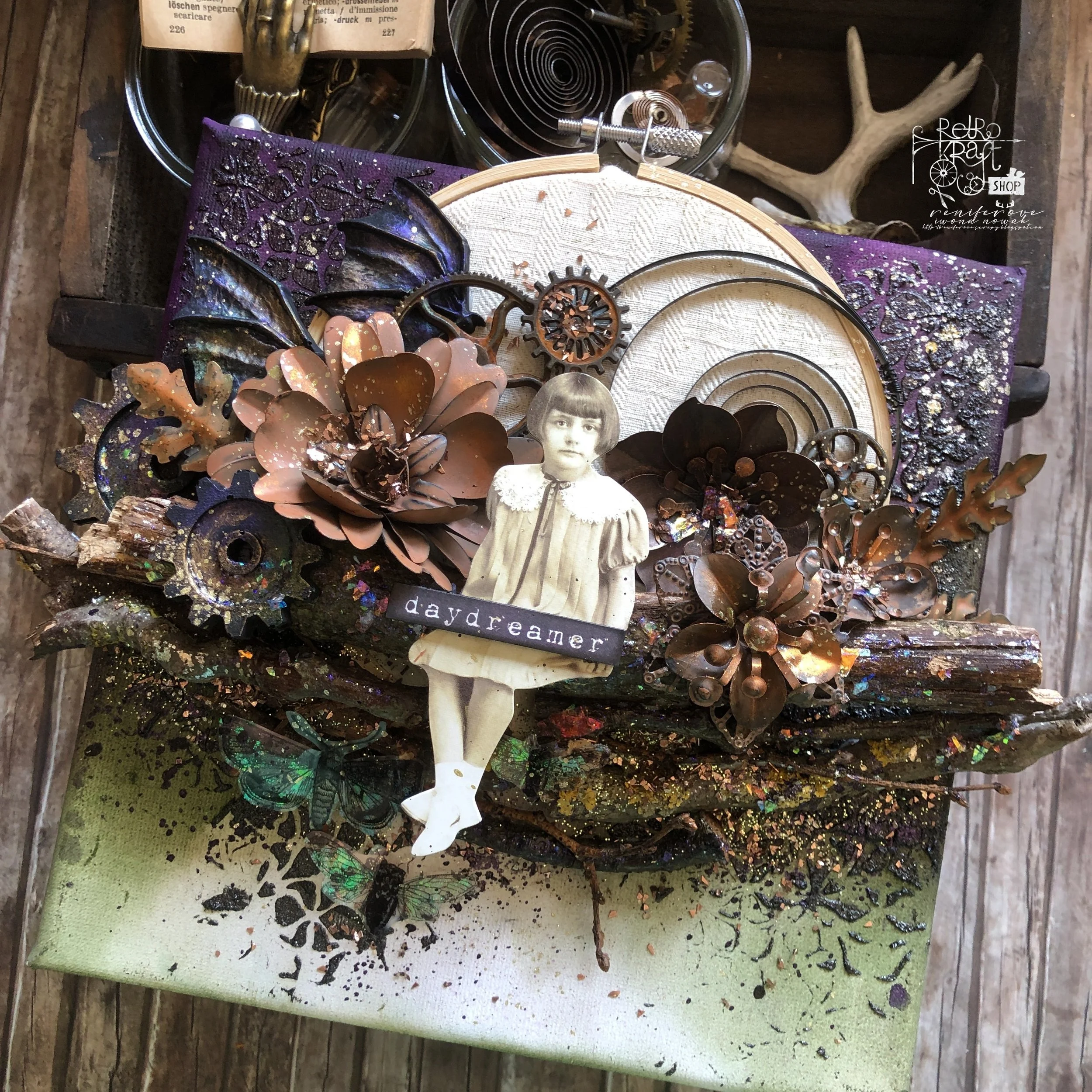 Mixed steampunk art project featuring metallic flowers, gears, and a vintage girl cutout with the word 'daydreamer', on a wooden surface with paint splatters.