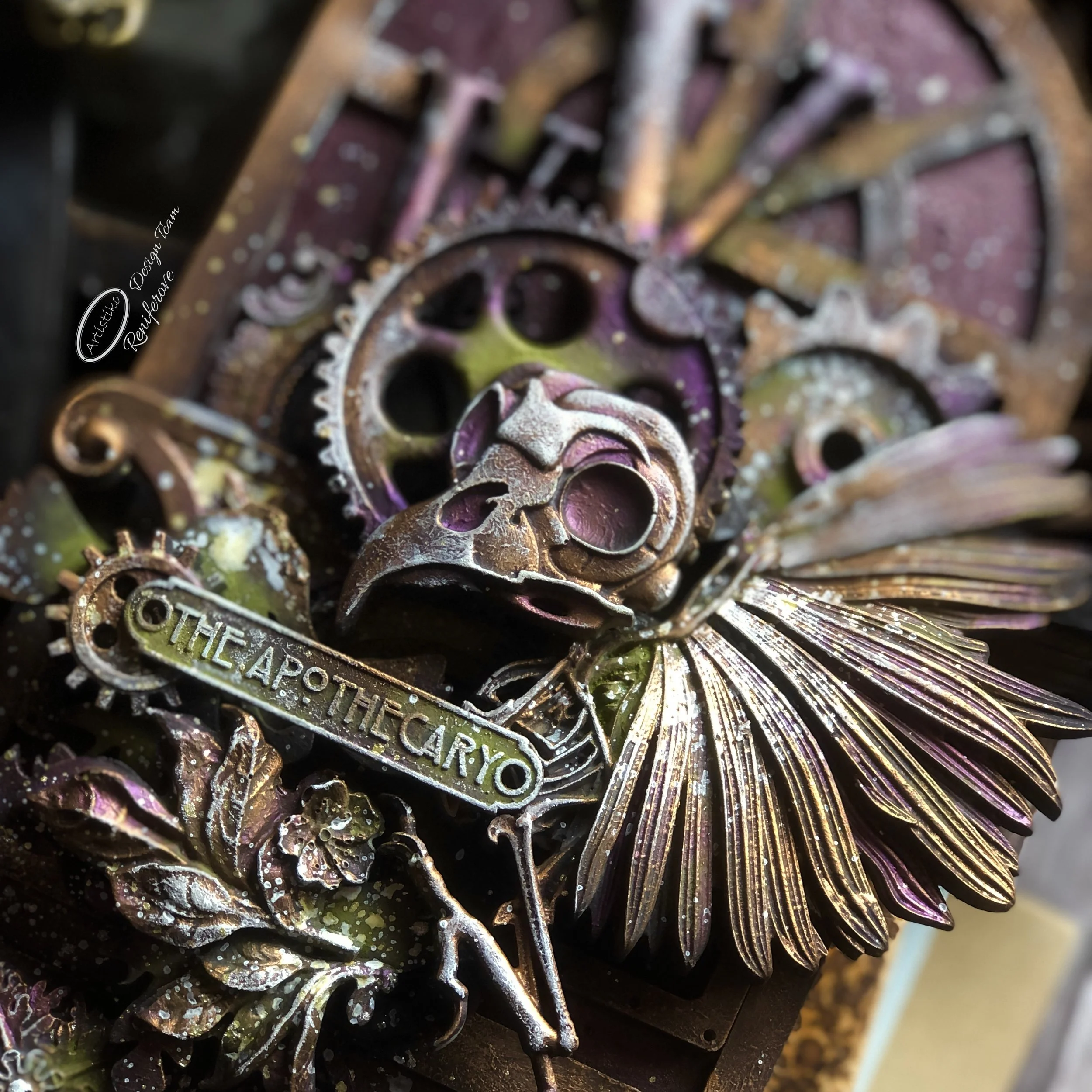 Close-up of a metallic art piece featuring a skull, gears, floral elements, and a banner that reads 'THE APOCALYPSE,' with a dark background.