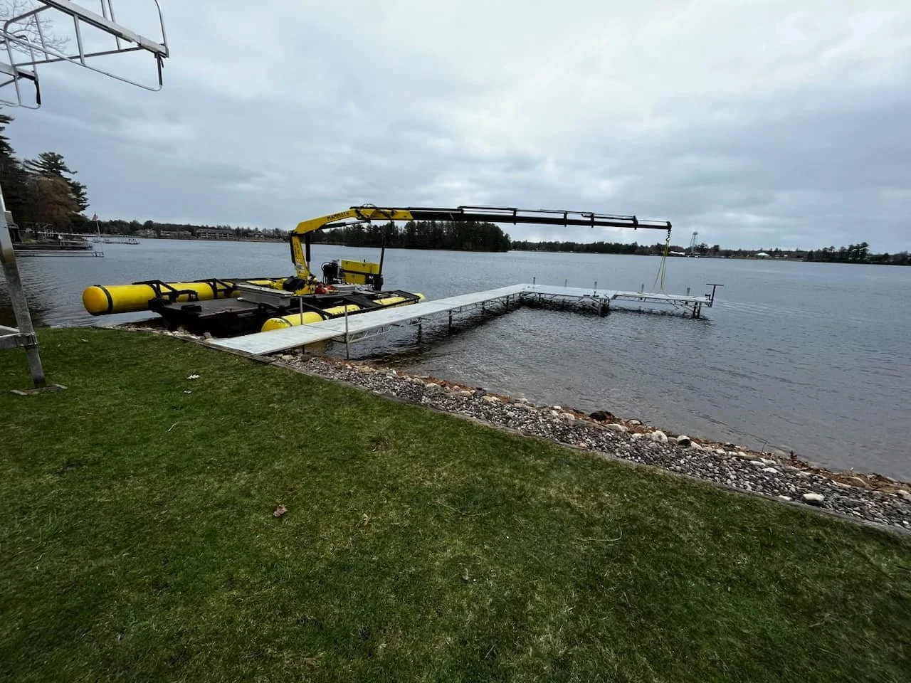 Large yellow underwater drone on a dock by a body of water, with a floating platform and cloudy sky.
