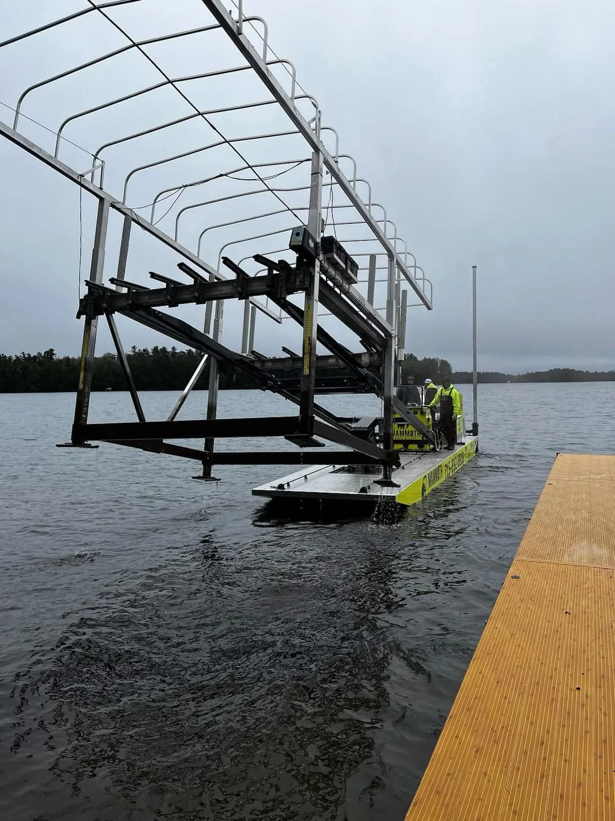 A drone is being launched from a floating platform into a body of water, with two individuals in safety vests and helmets present.