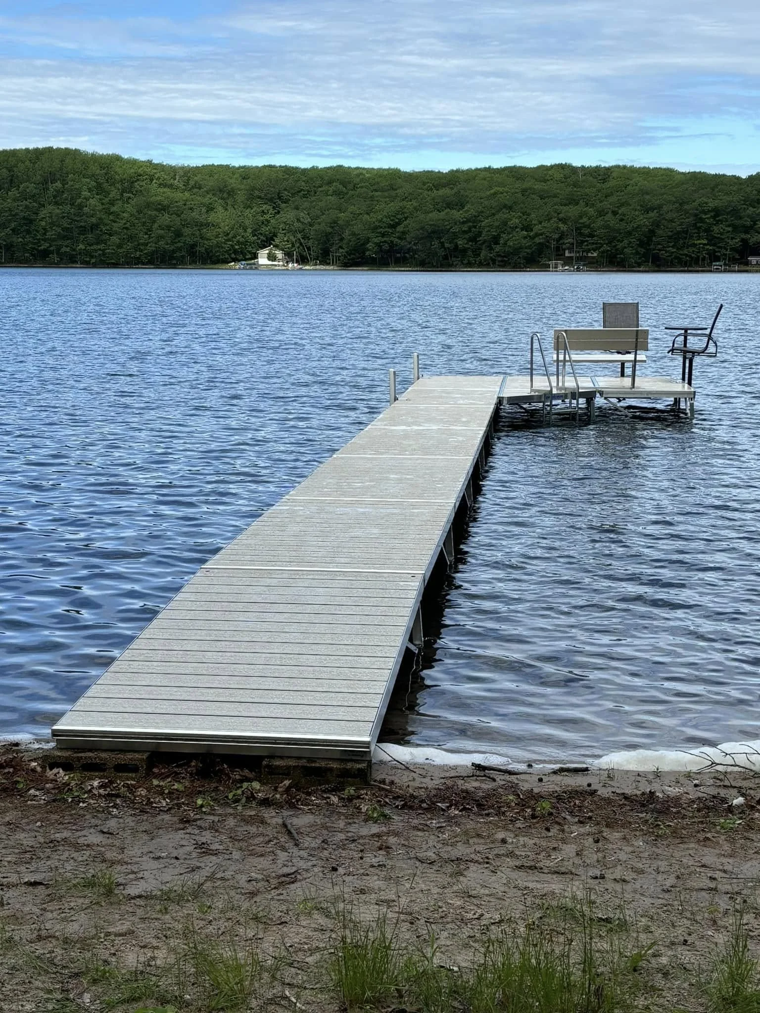 Dock extending into a lake with chairs on it, surrounded by water and trees in the background.