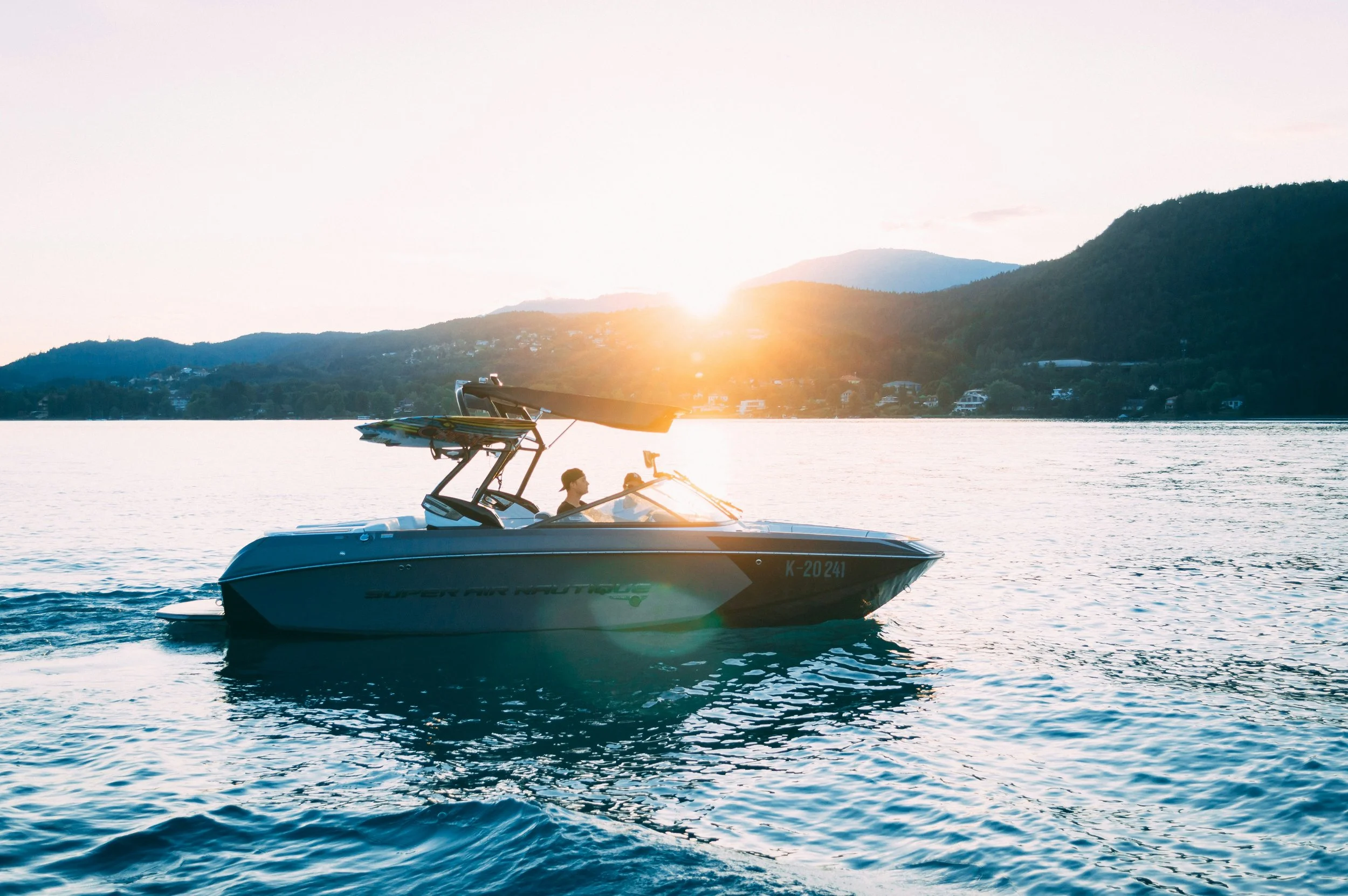 A speedboat on the water during sunset, with a person at the helm and mountains in the background.