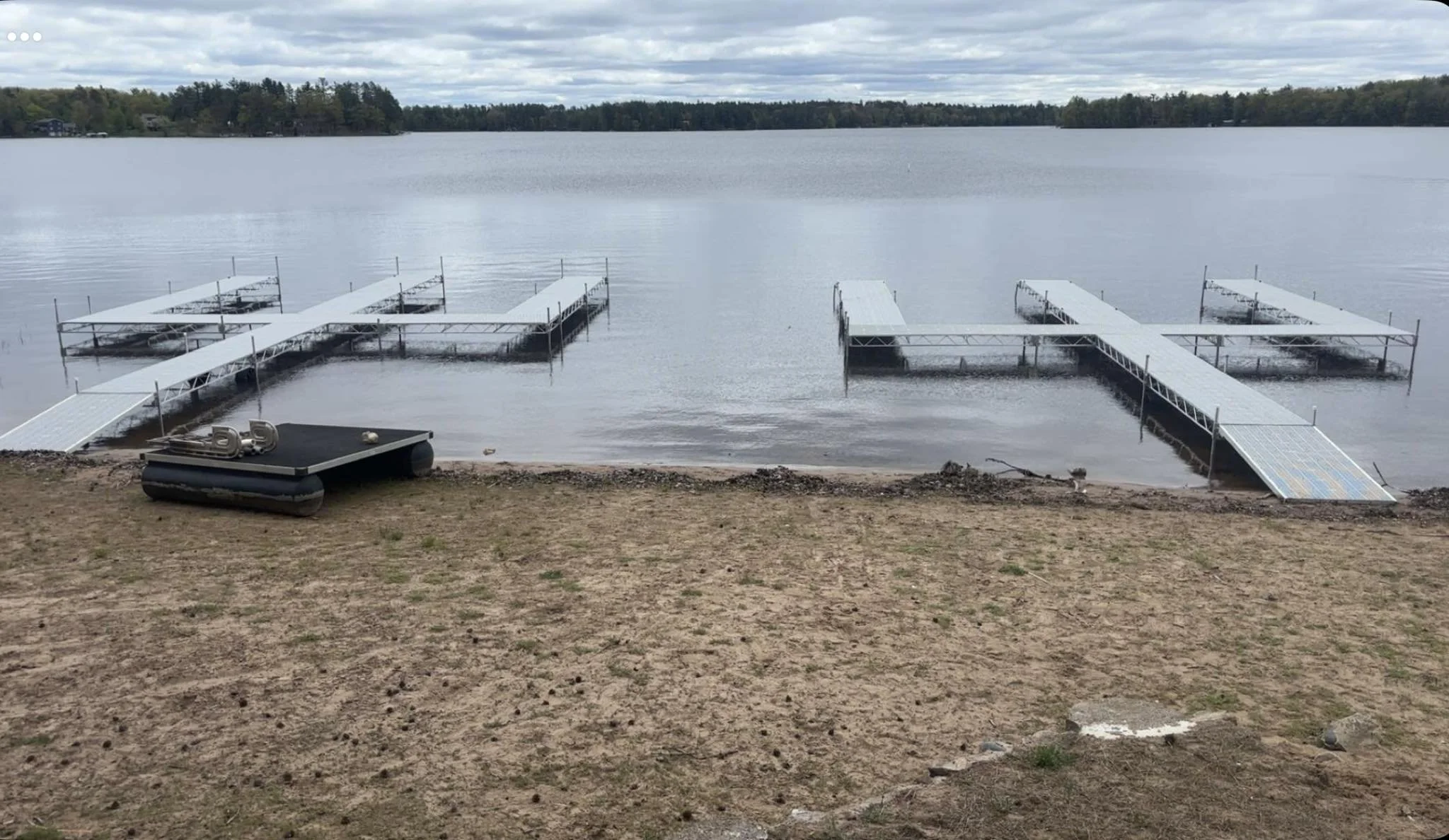 A lakeside view showing two floating docks connected to the shore with ramps, under a cloudy sky.