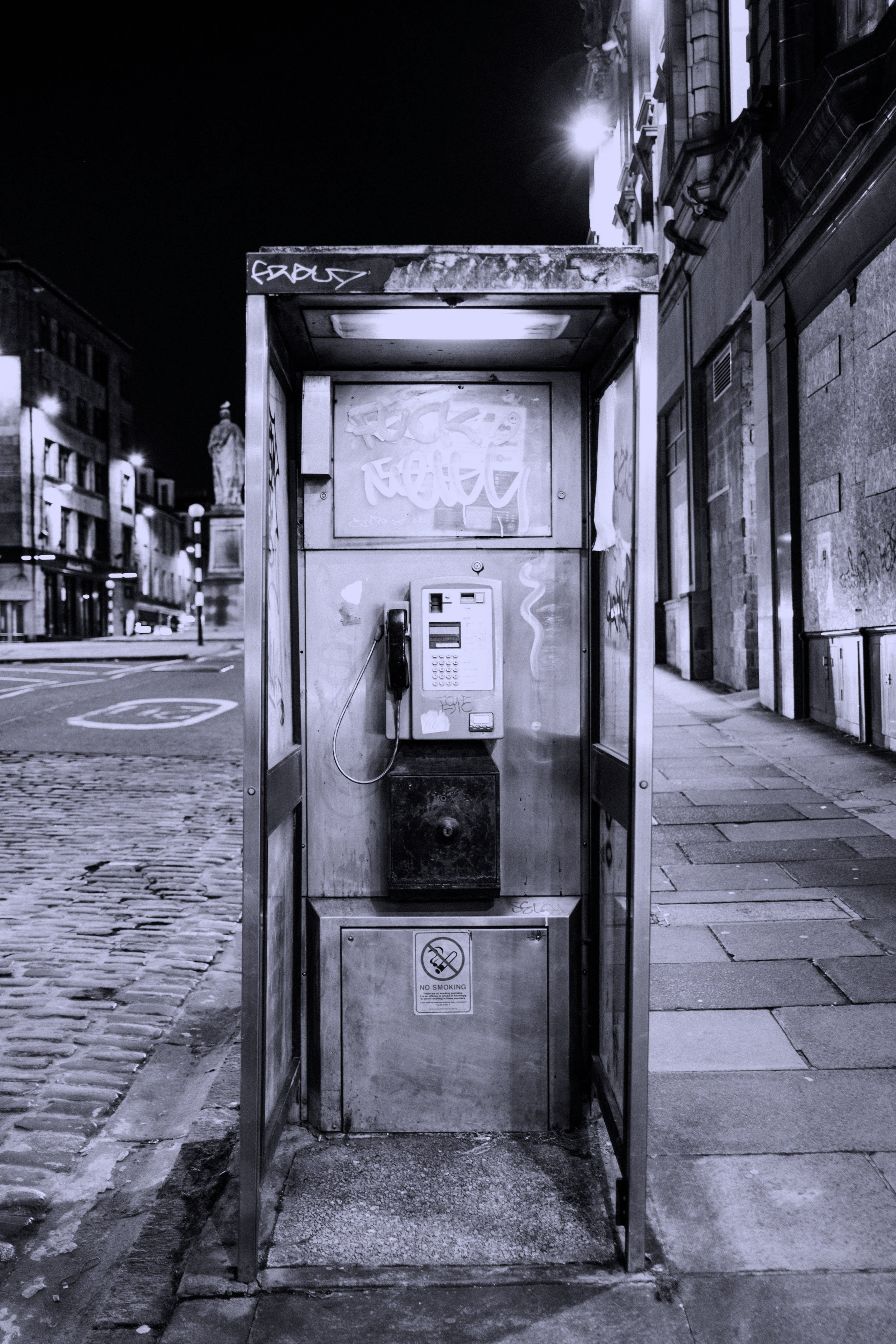 Empty payphone booth on a city street at night with graffiti, no people visible.