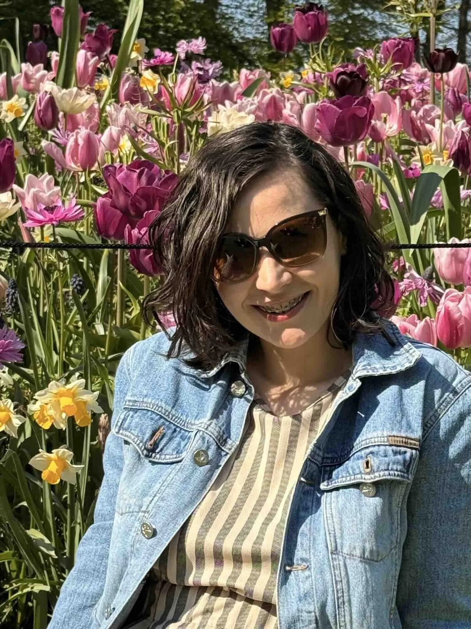 Mihaela Calin smiling in a vibrant field of spring tulips in Amsterdam, representing the person behind Bridges and Anchors therapy.