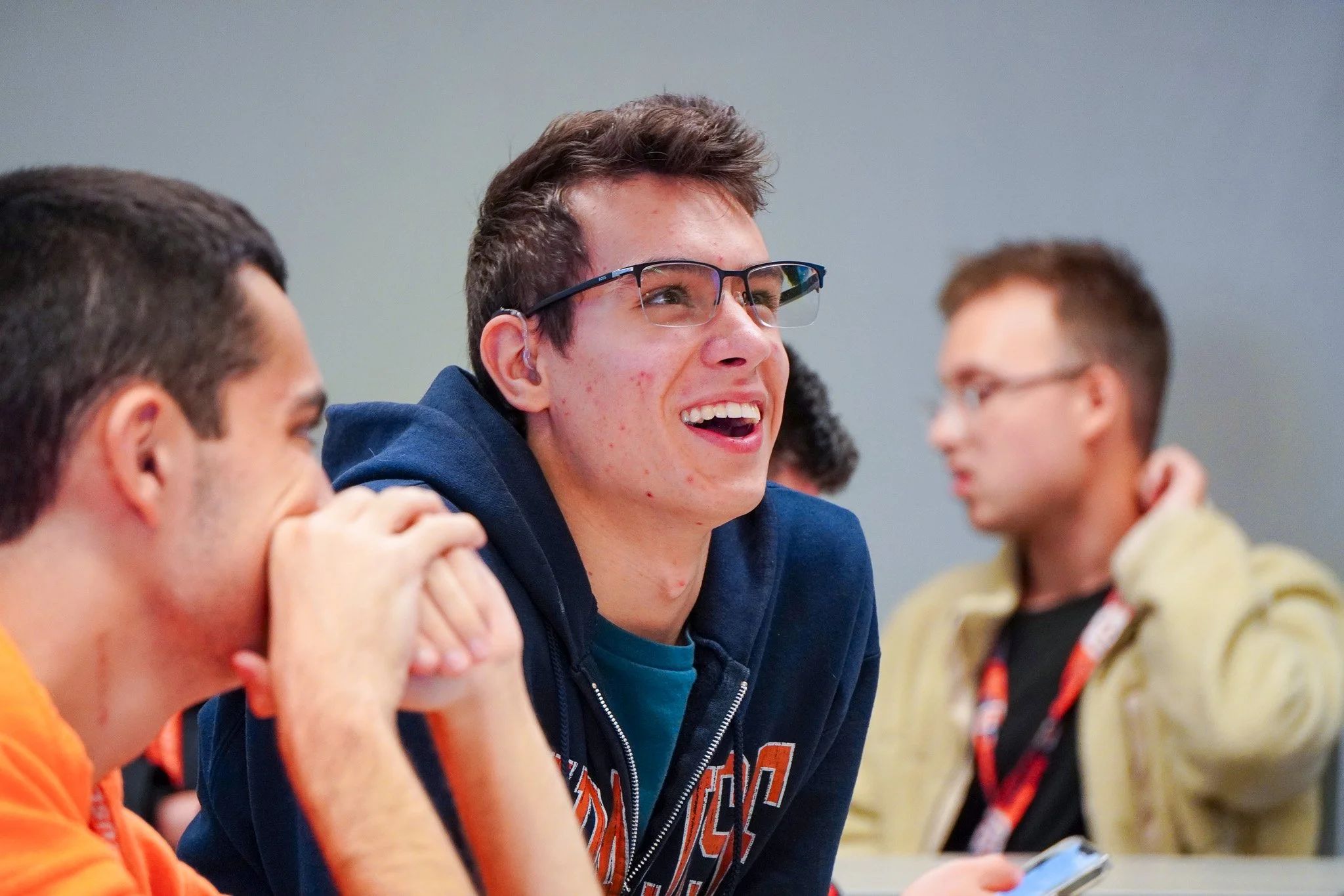 A group of young men sitting together, smiling, and engaging in conversation in an indoor setting.