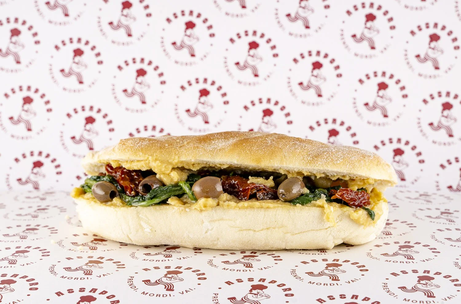 Panino con crema di ceci, cicoria, pomodori secchi e olive taggiasche.