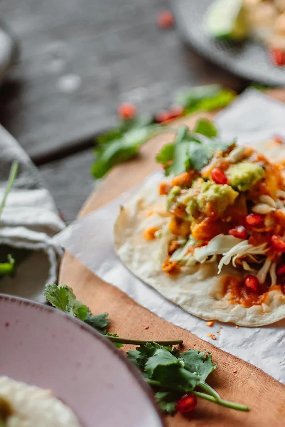Close-up of a taco with shredded vegetables, guacamole, and cilantro on a wooden cutting board.