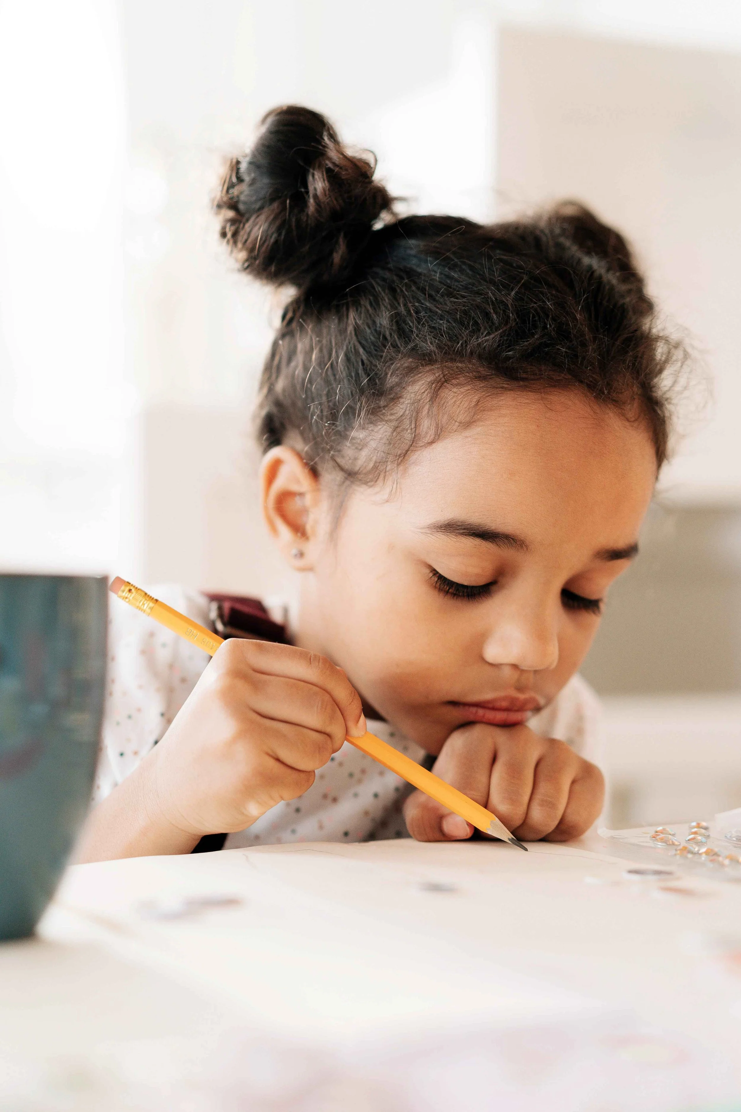 Young child concentrating while drawing with a pencil at a table.