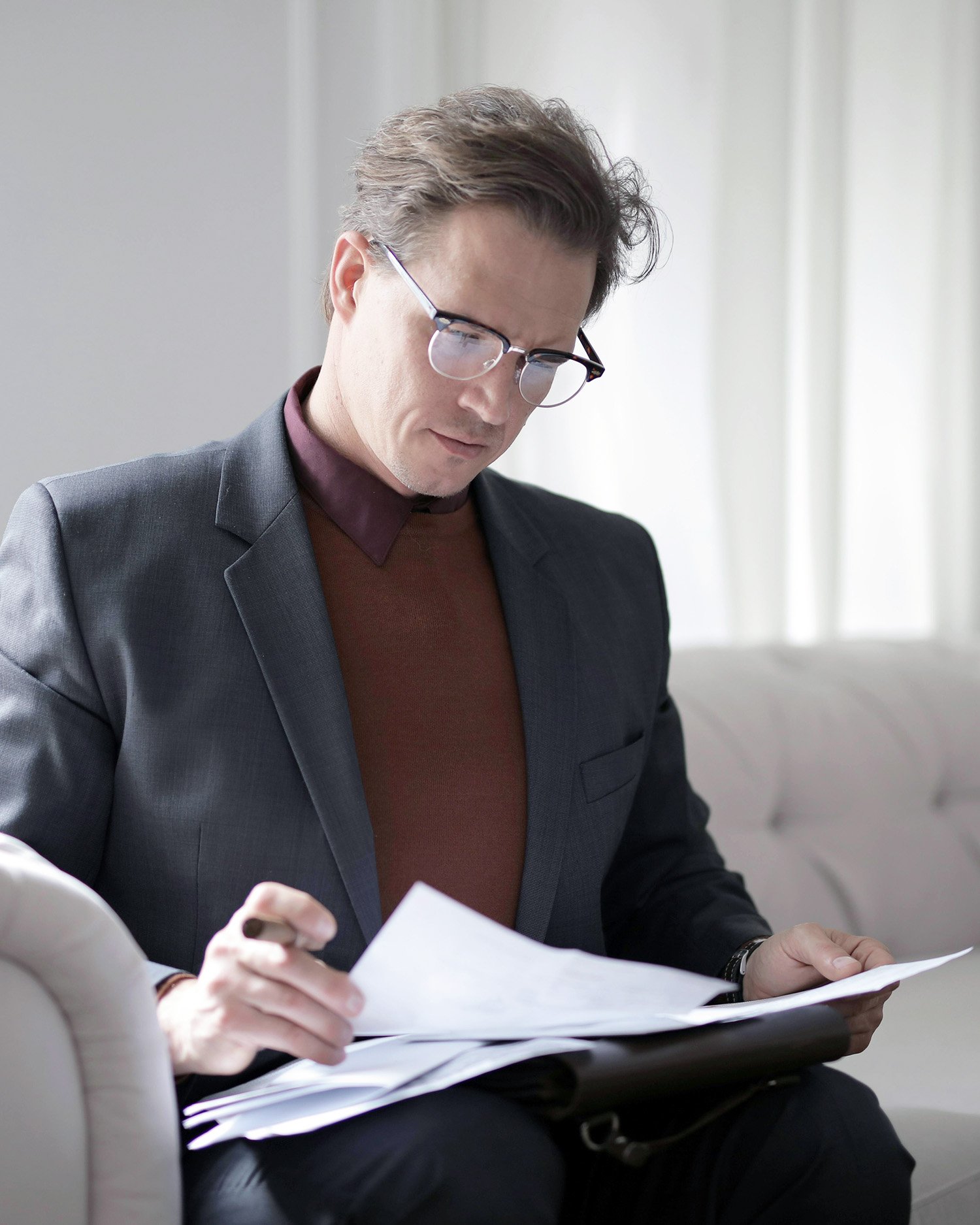 Man wearing glasses reviewing documents while seated, focused and reading papers in a professional setting.
