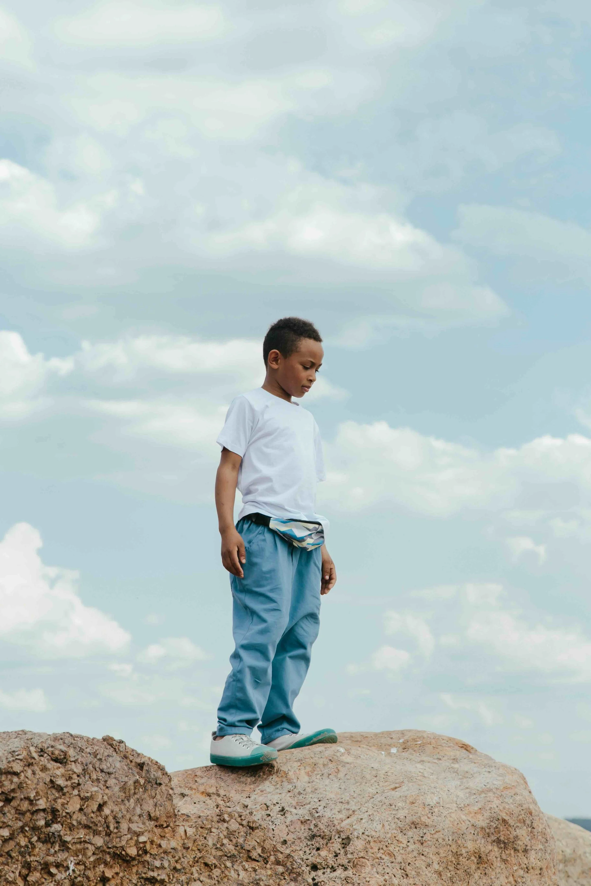 Young child standing on a rock under a cloudy sky.