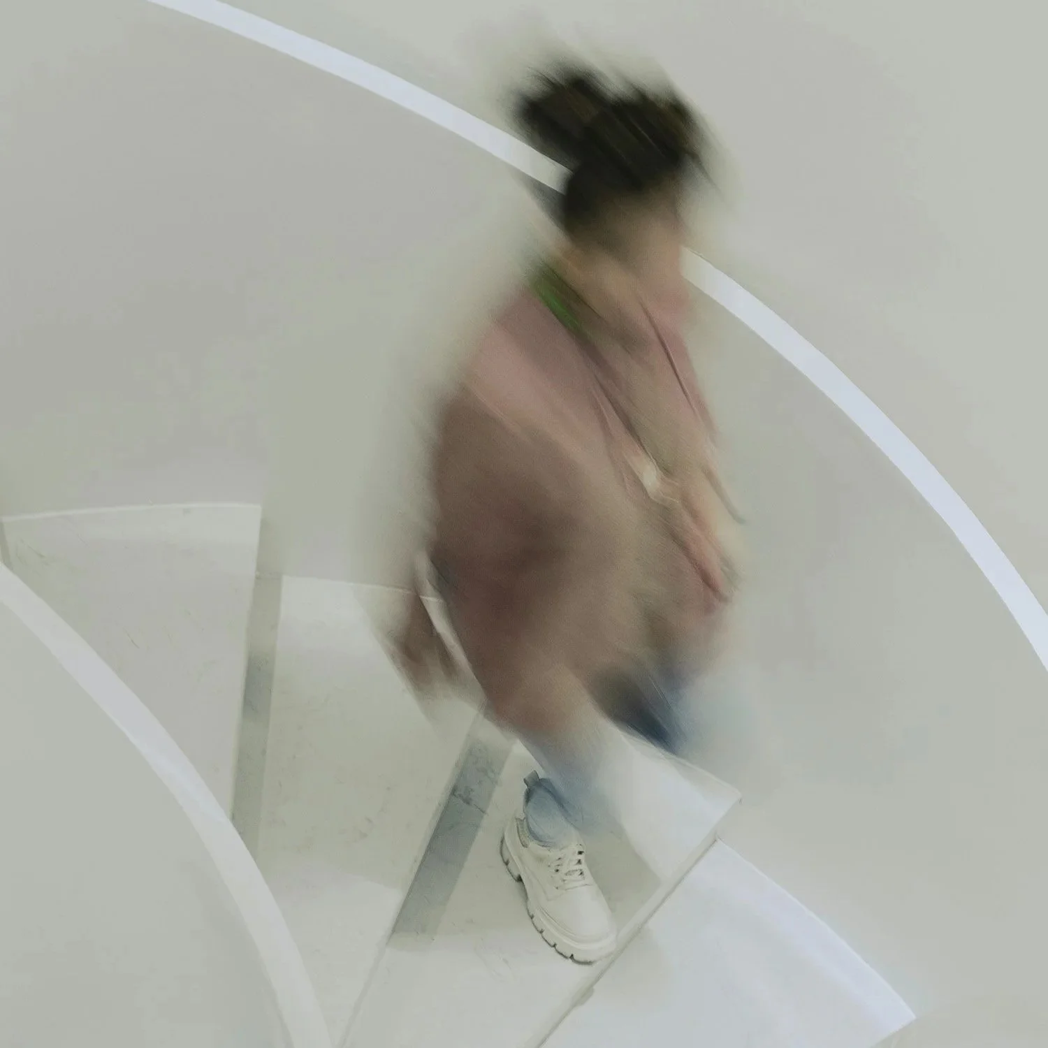 Blurred figure walking down a curved white staircase viewed from above.