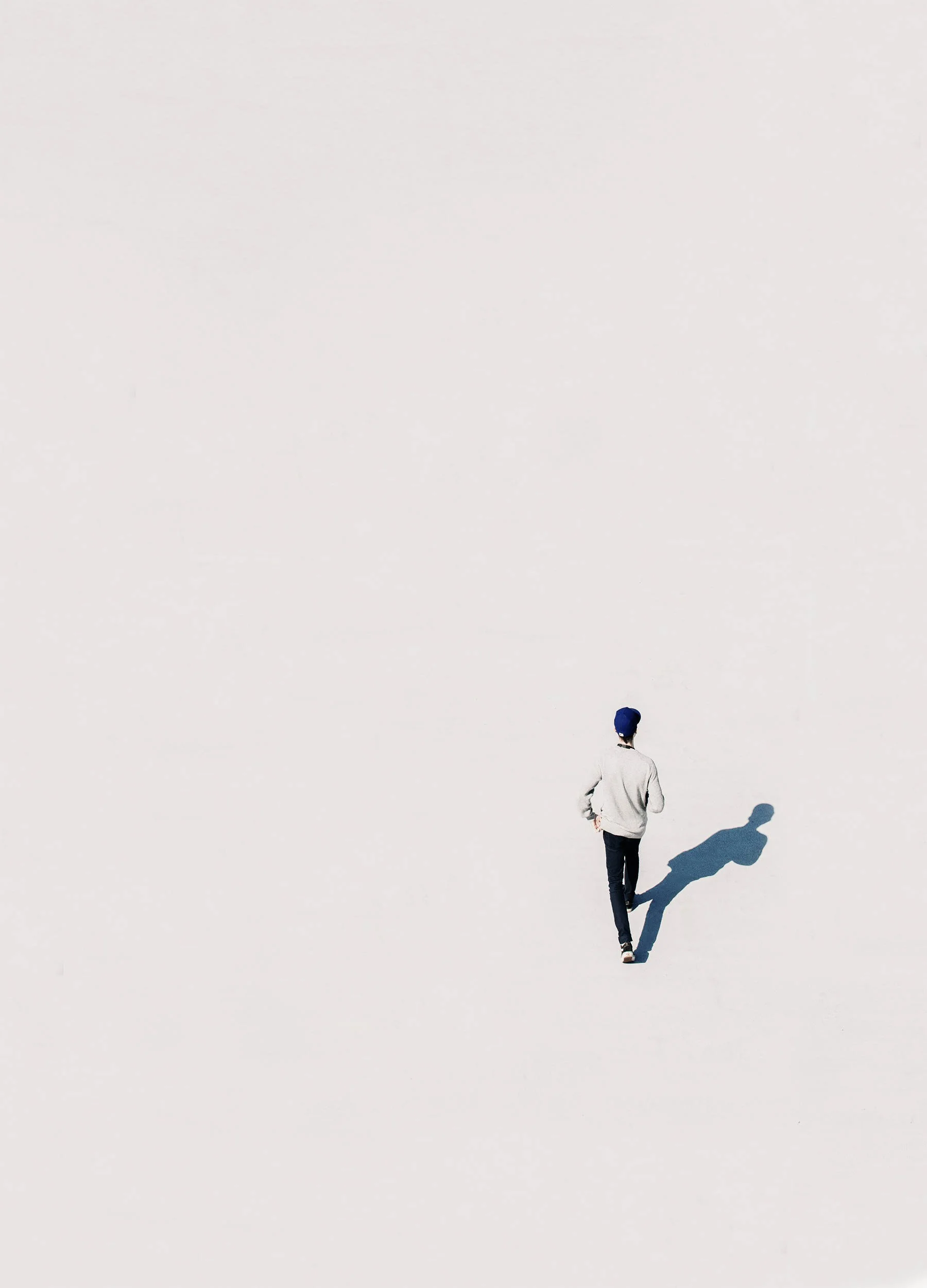 Person walking alone across a wide empty pale surface casting a long shadow.