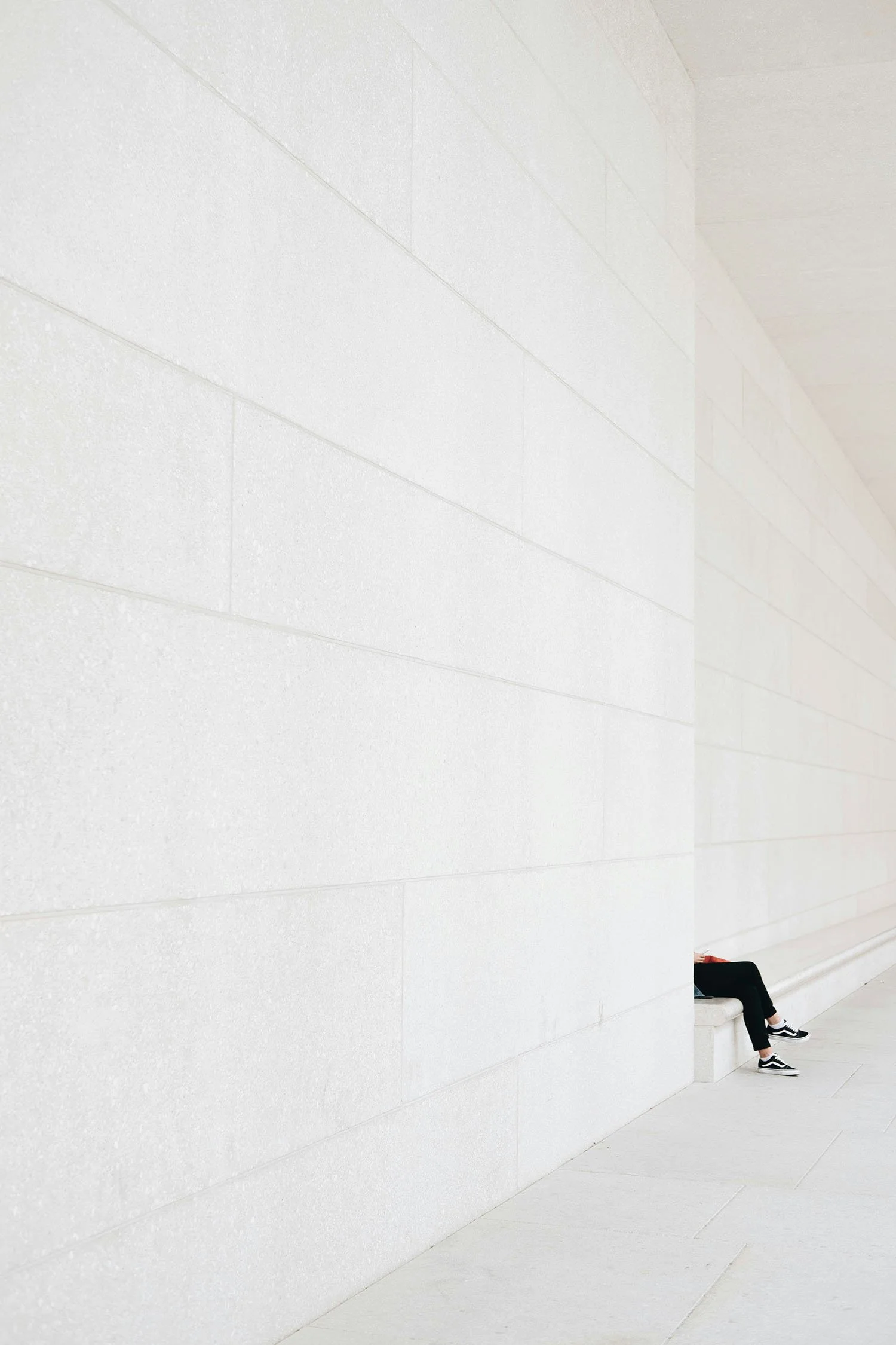 Long minimalist white wall with a person seated at the far end, creating a sense of scale and openness.
