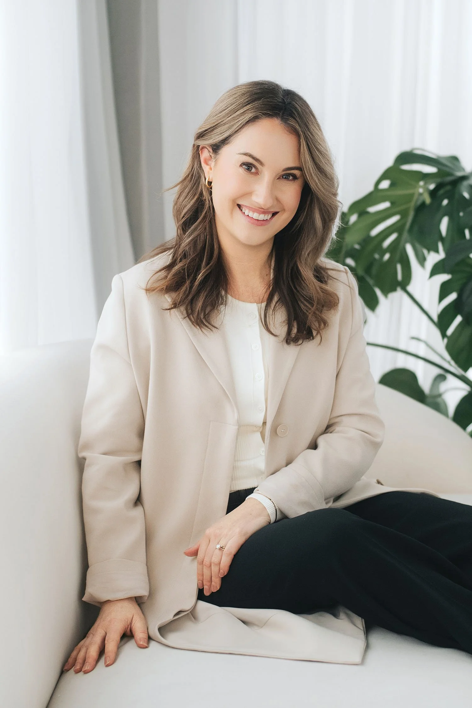 Portrait of psychologist Dr. Lauren Campbell smiling, wearing a beige blazer and seated near a window with a green plant in the background.