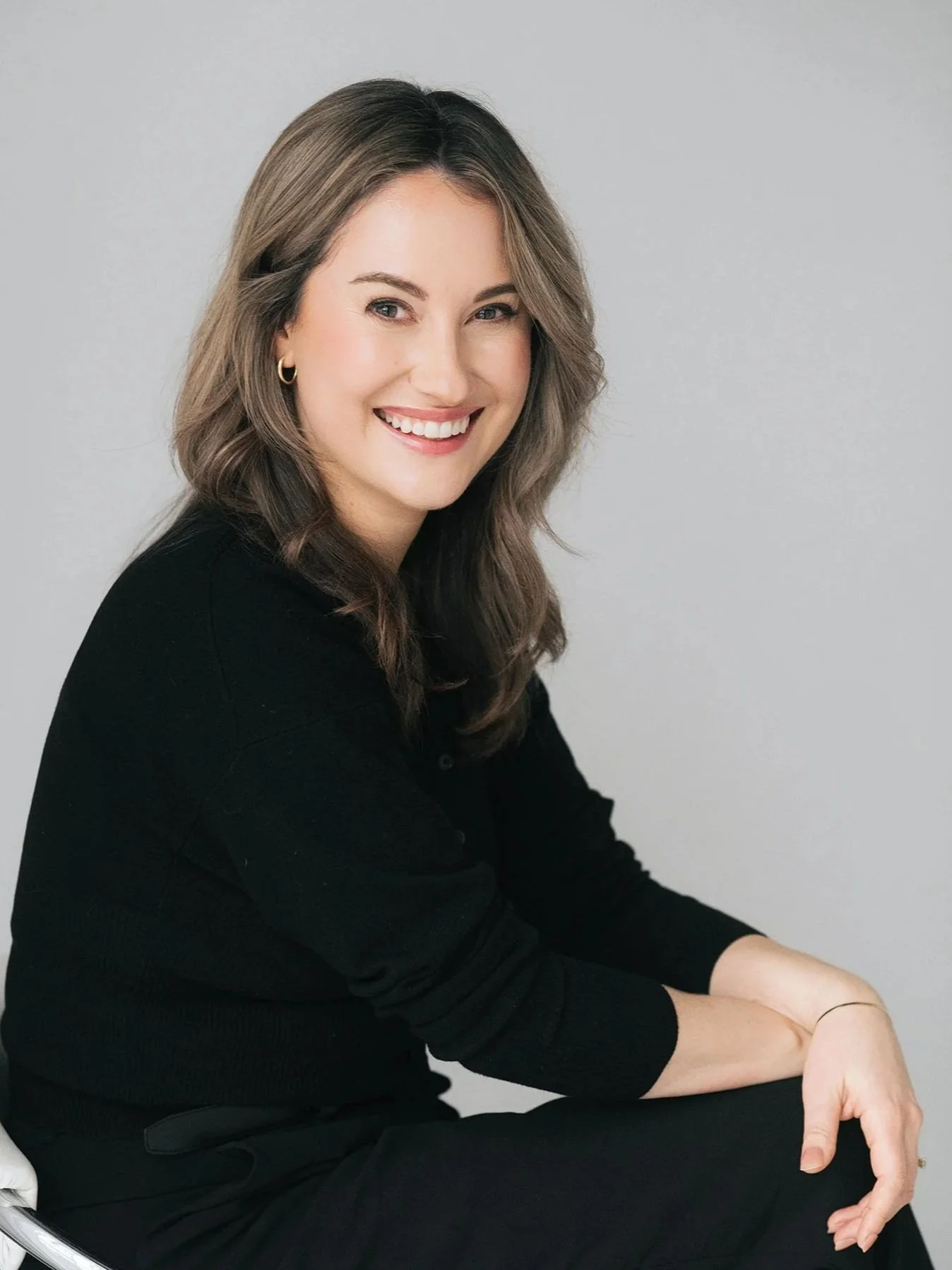 Portrait of Dr. Lauren Campbell, psychologist, with shoulder-length brown hair wearing a black top, seated and facing slightly sideways against a soft neutral background.