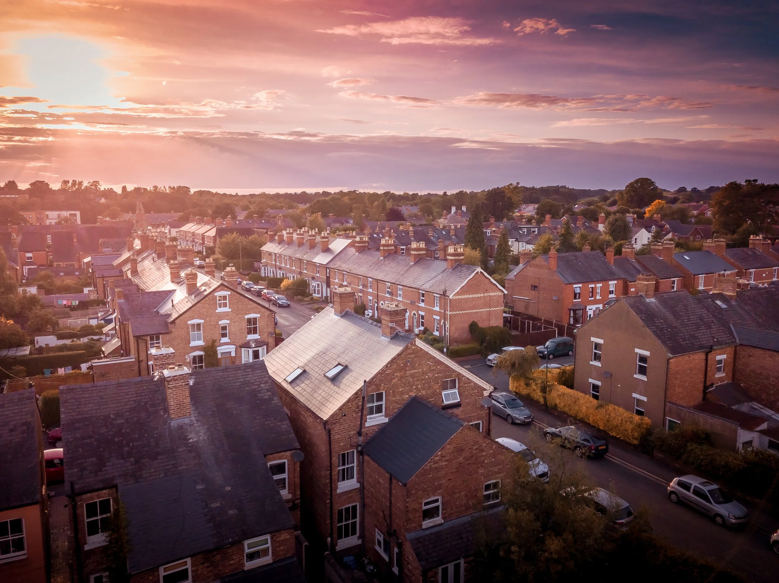 Aerial view of a residential neighborhood at sunset with brick houses and parked cars.